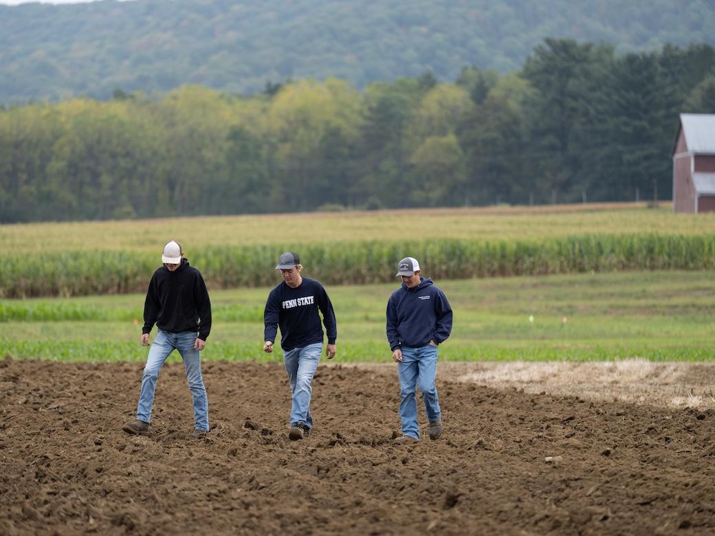 Three students walk across a farm field.