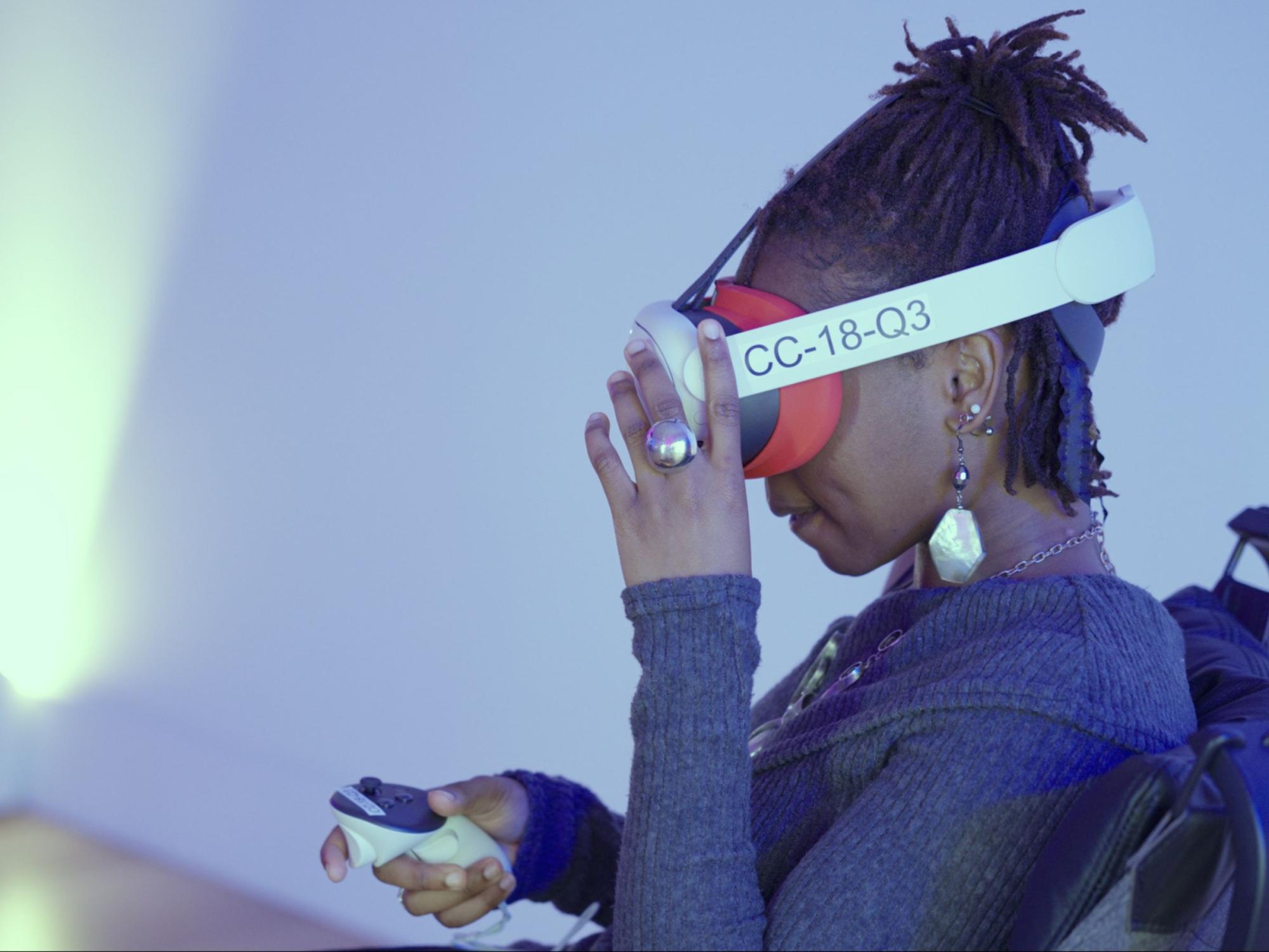 dark-haired person wears virtual reality headset and holds controller