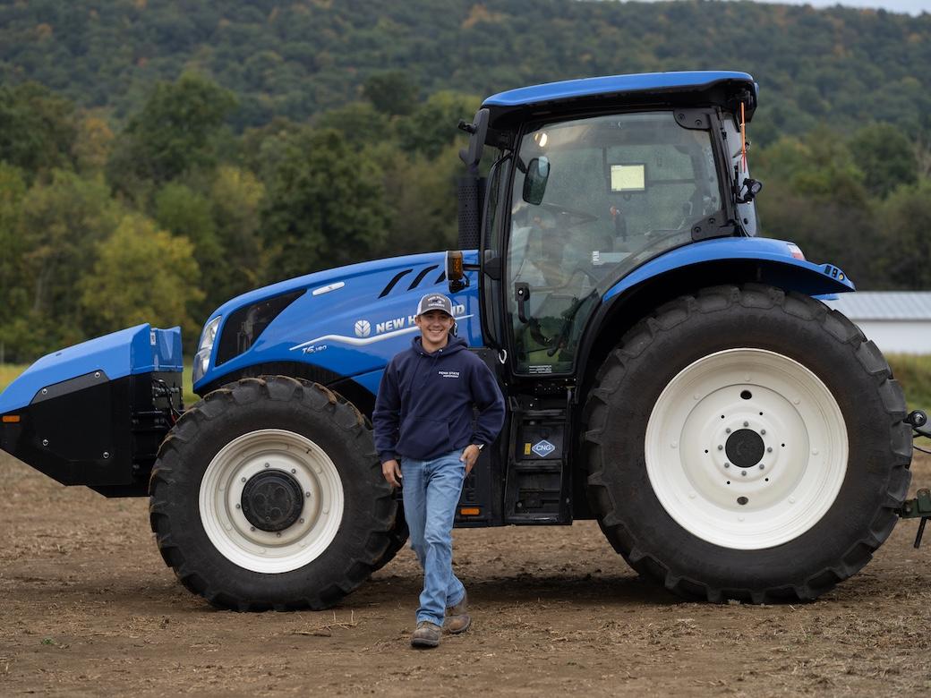 Penn State student Eric Weaver walks away from the large blue tractor that sits in a field.