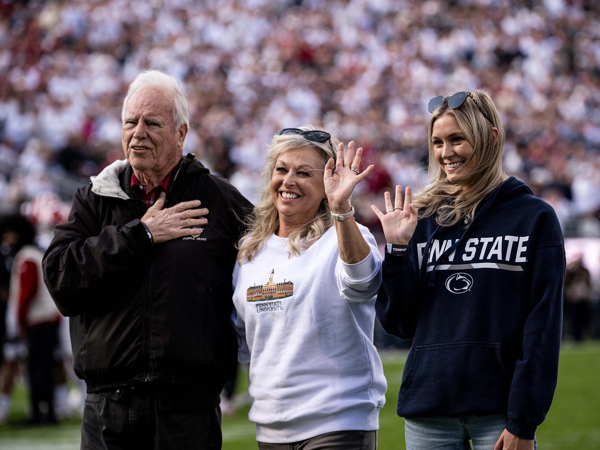 Three people stand on a football field in a crowded stadium.