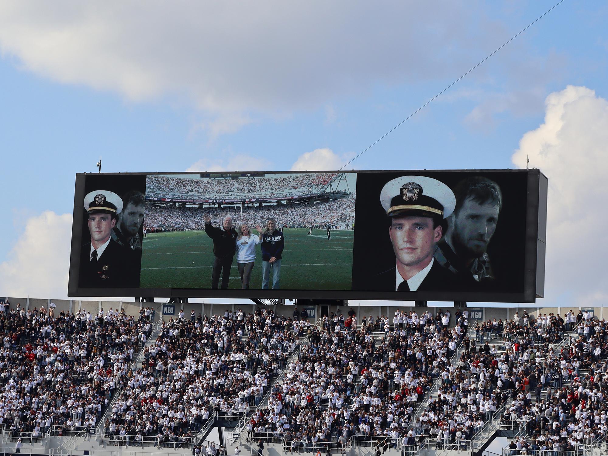 A large digital screen with a family waving in a stadium.