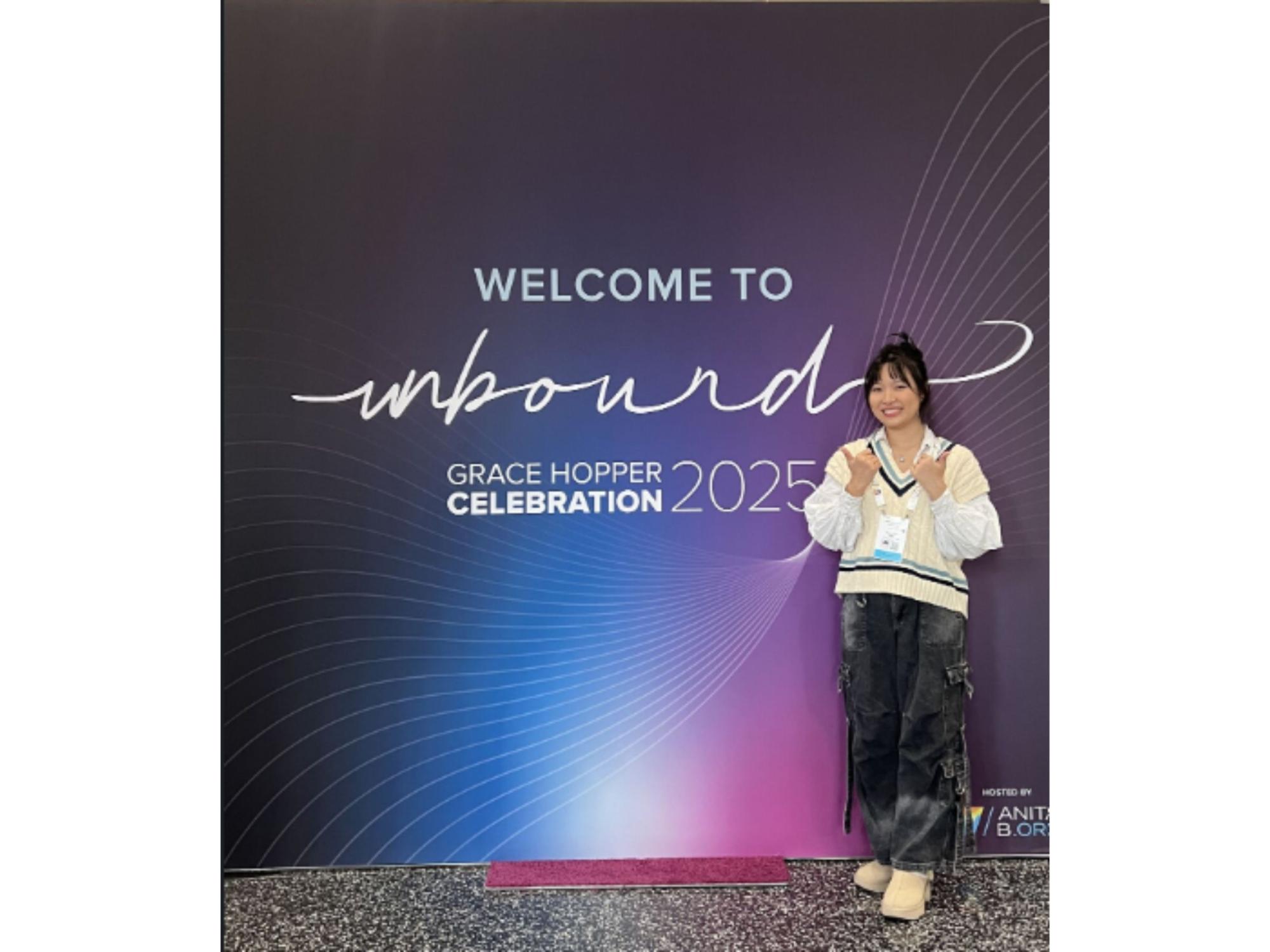 dark-haired person poses next to large conference sign