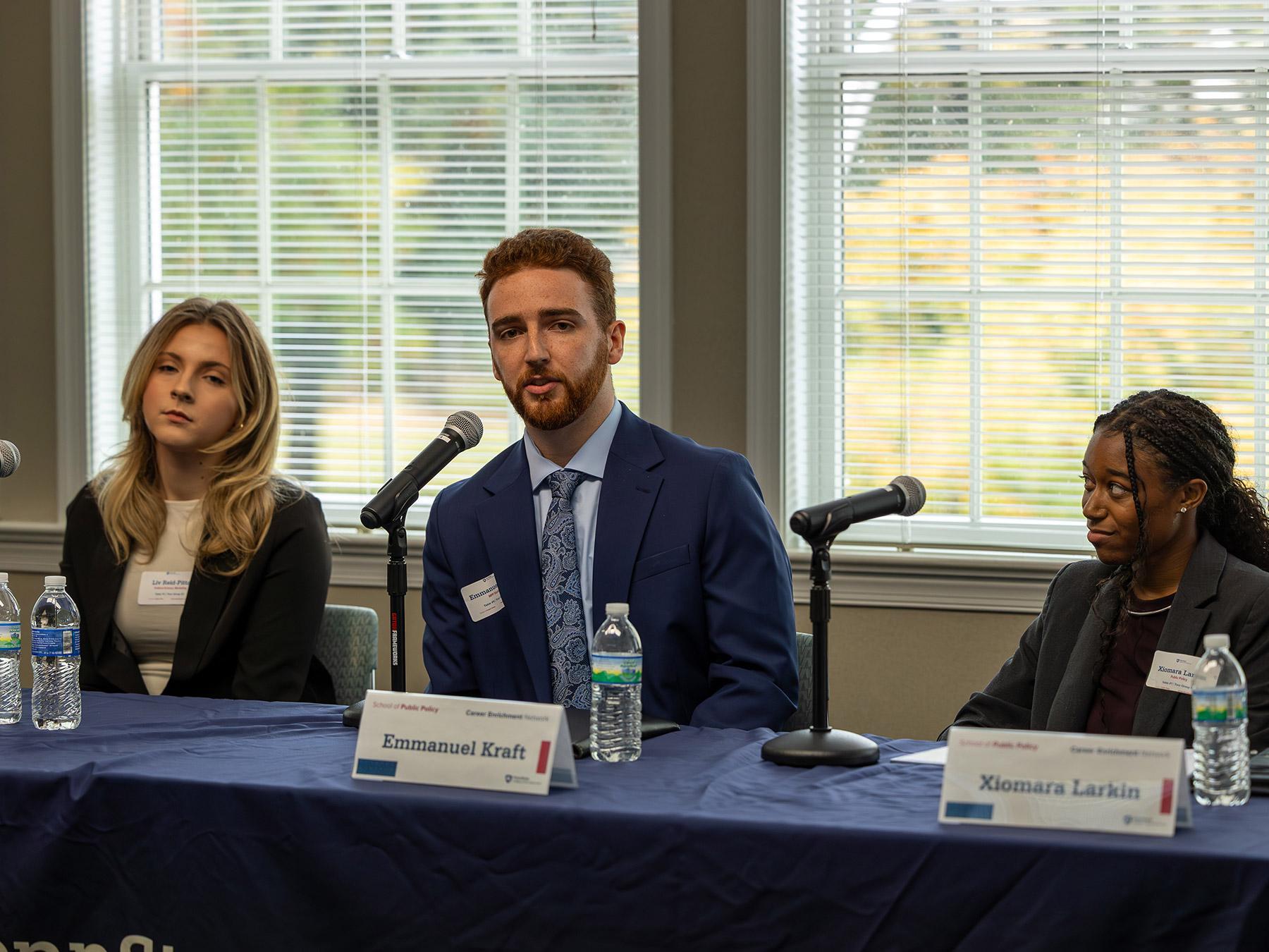 Three students sit at a table outfitted with microphones