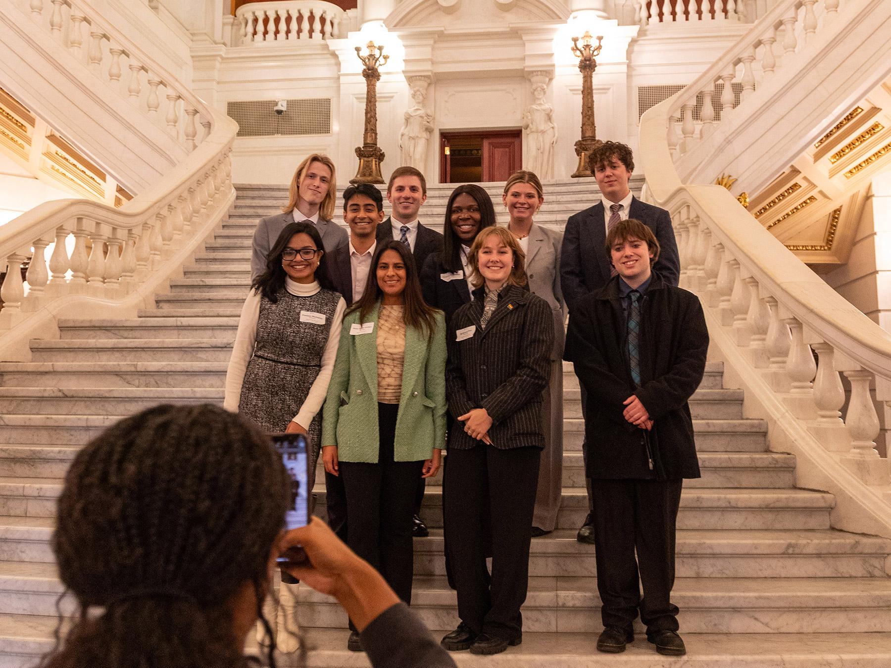 A group of students poses for a photo on the marble steps inside the Capitol building