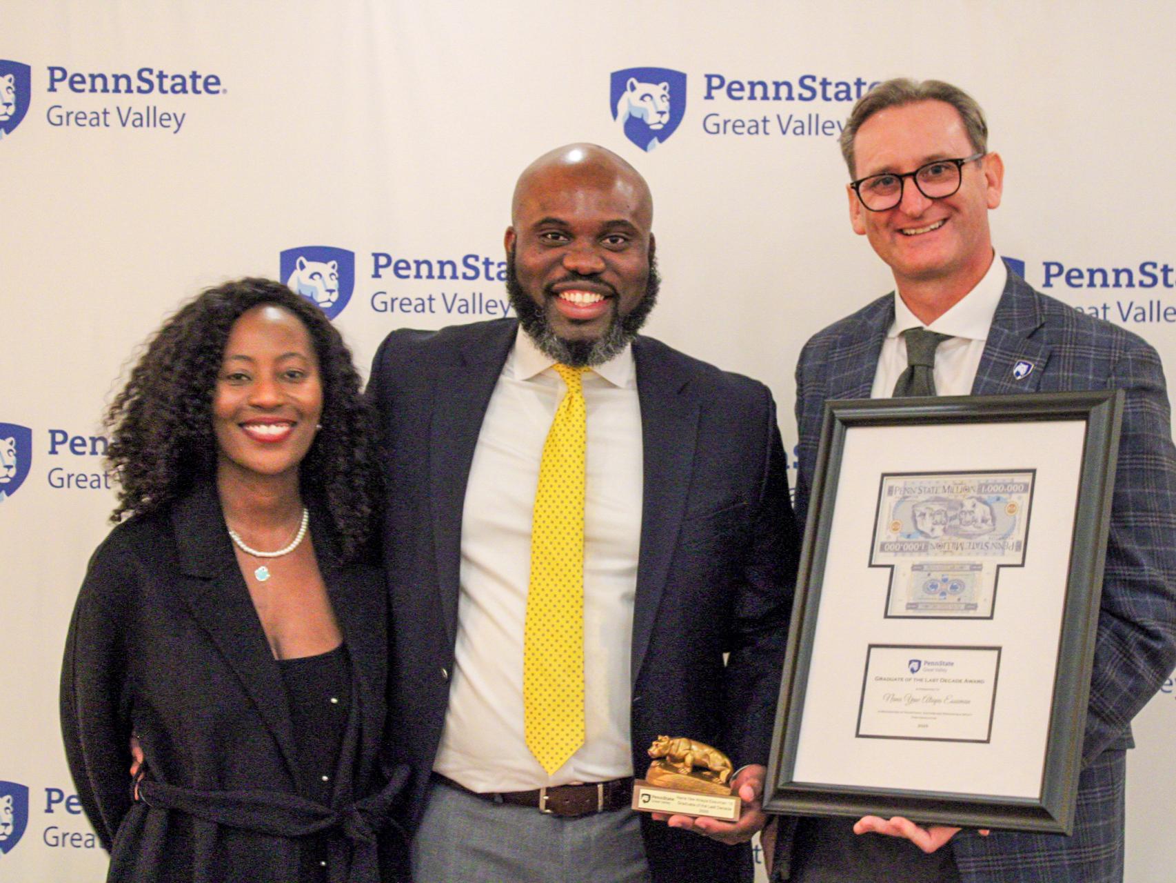 An alumnus and his wife receive an award plaque from the chancellor.