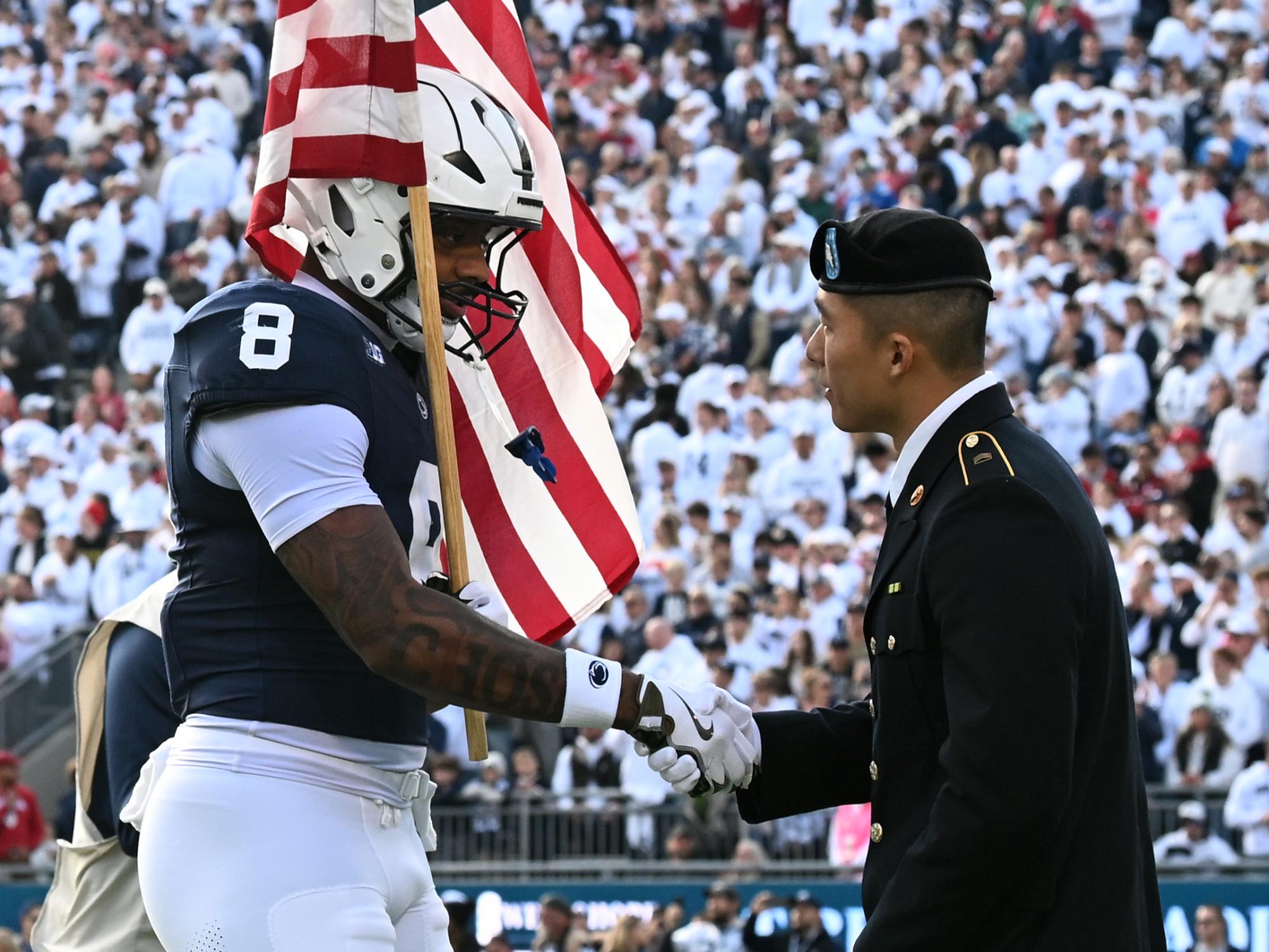 Football player holding flag shaking hands with ROTC cadet