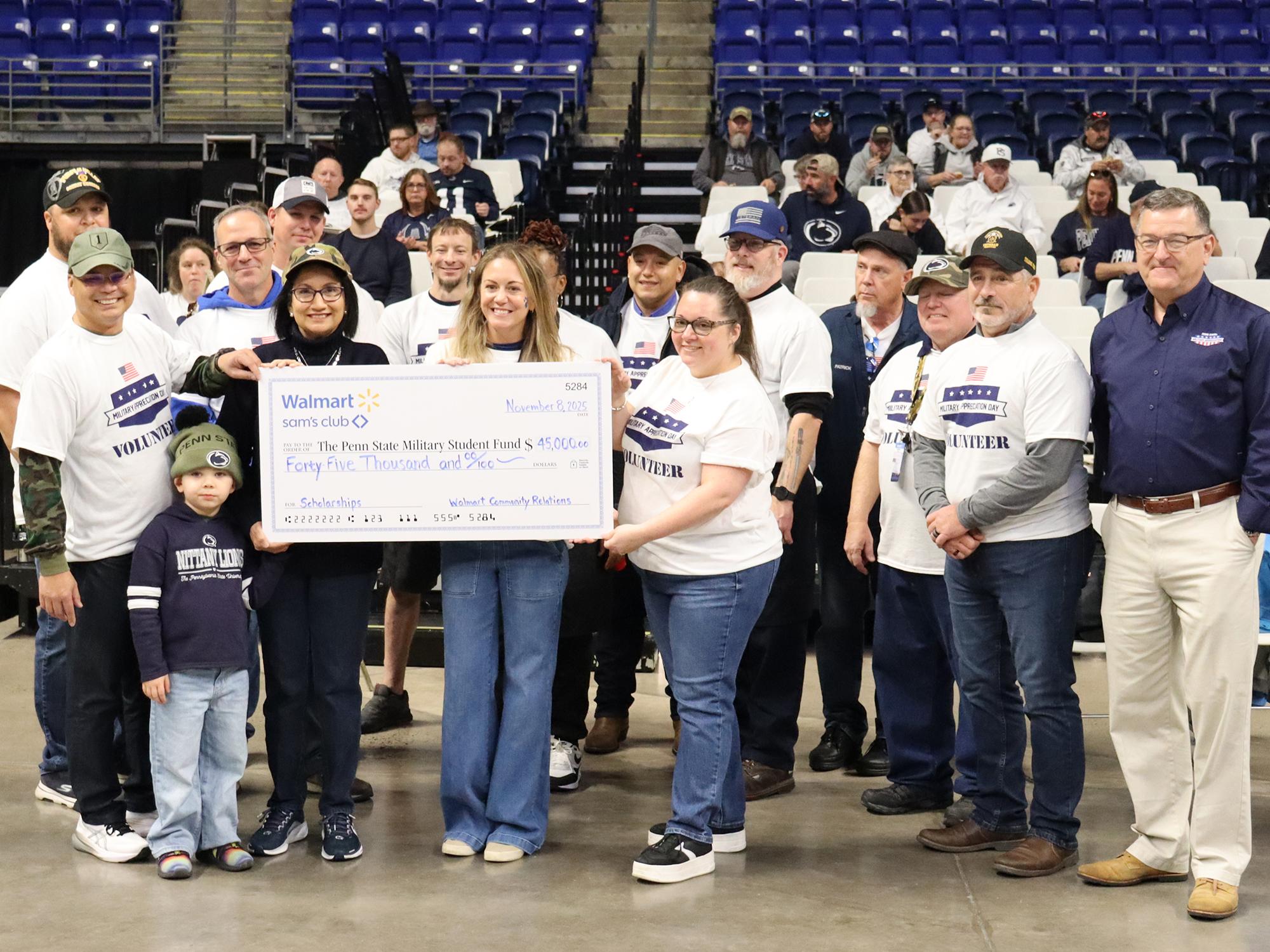 A group of people pose for a photo with a large check inside an arena.