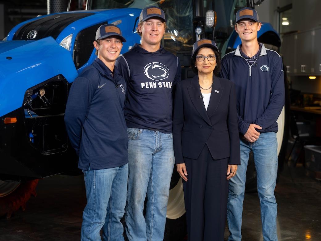 Three students and Neeli Bendapudi stand together in front of a large blue tractor.
