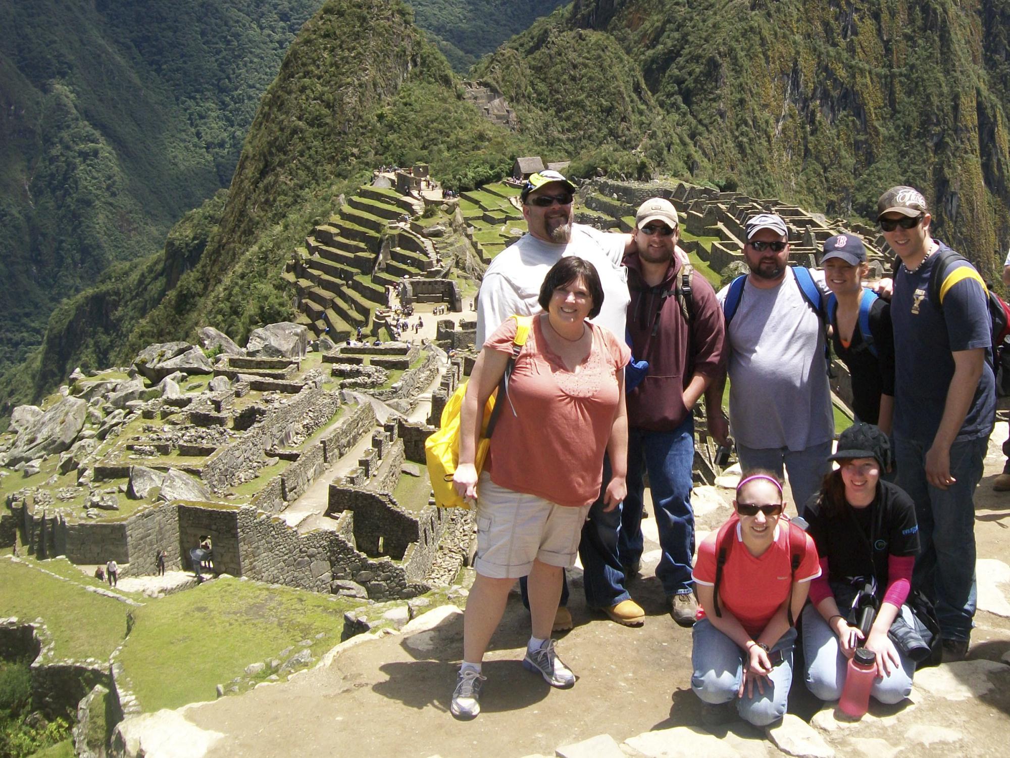 Eight people pose for a photo overlooking the historic ruins of Machu Picchu.