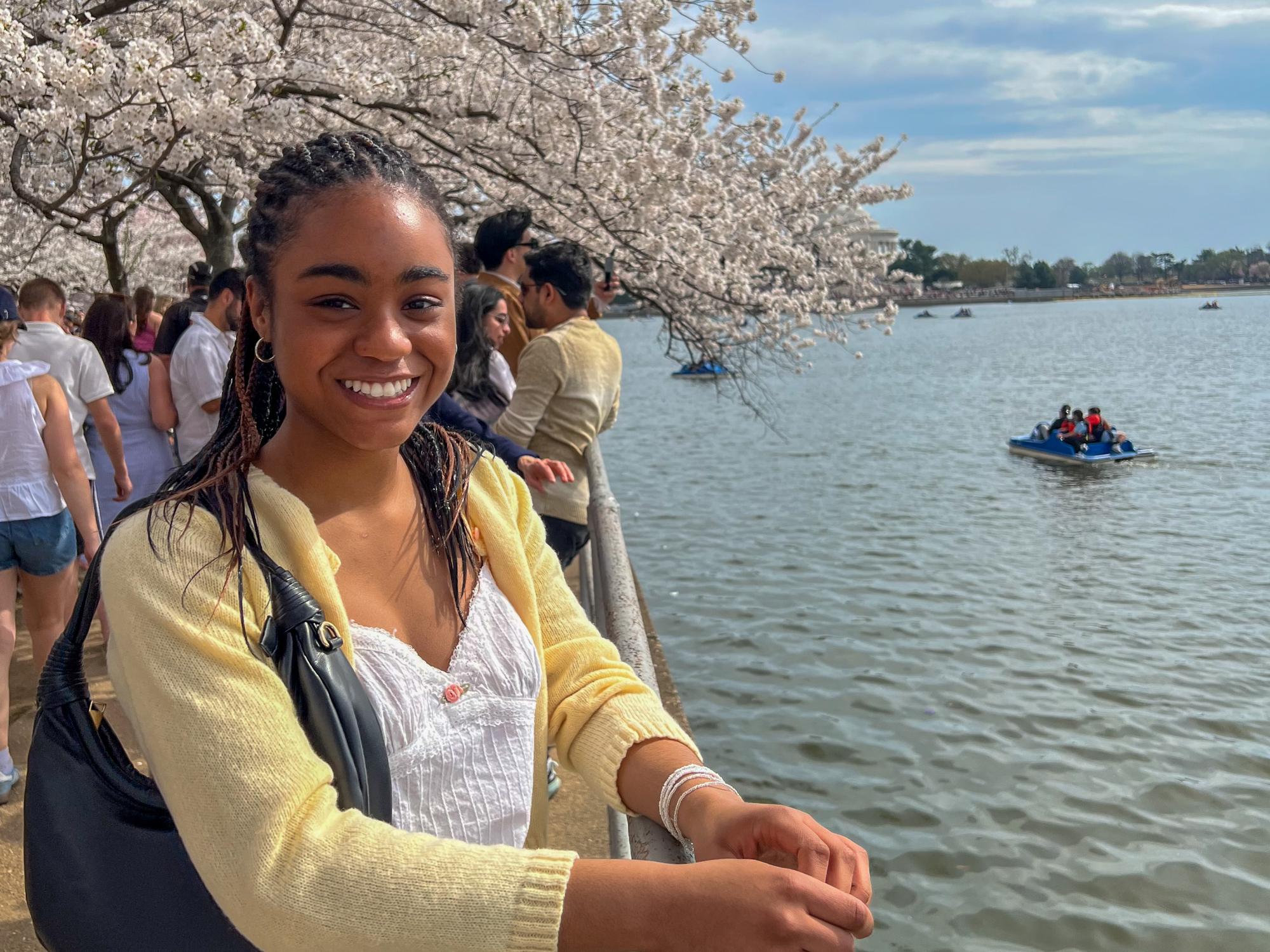 Simone Warren stands beside the Tidal Basin, with a cherry blossom tree in the background along the in Washington, D.C.