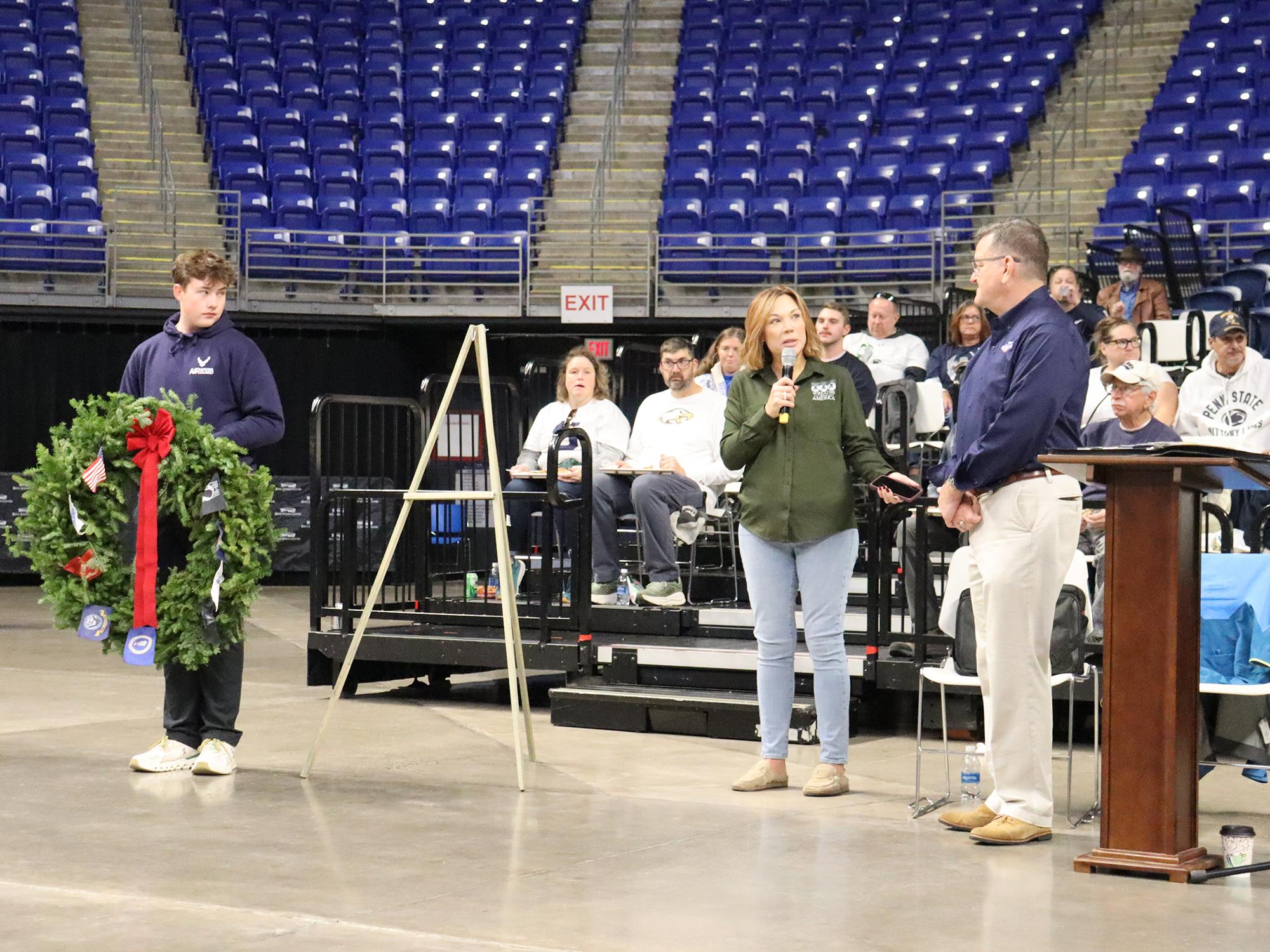 People in an area, one holding a wreath while other speak.