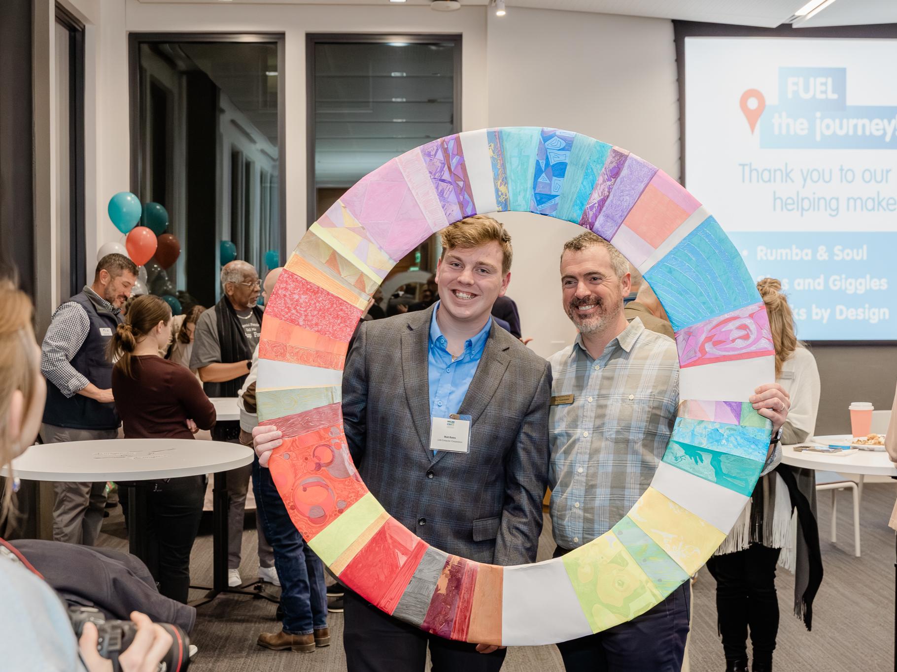 Two individuals pose holding up a large, GEW-themed colorful circle to frame themselves