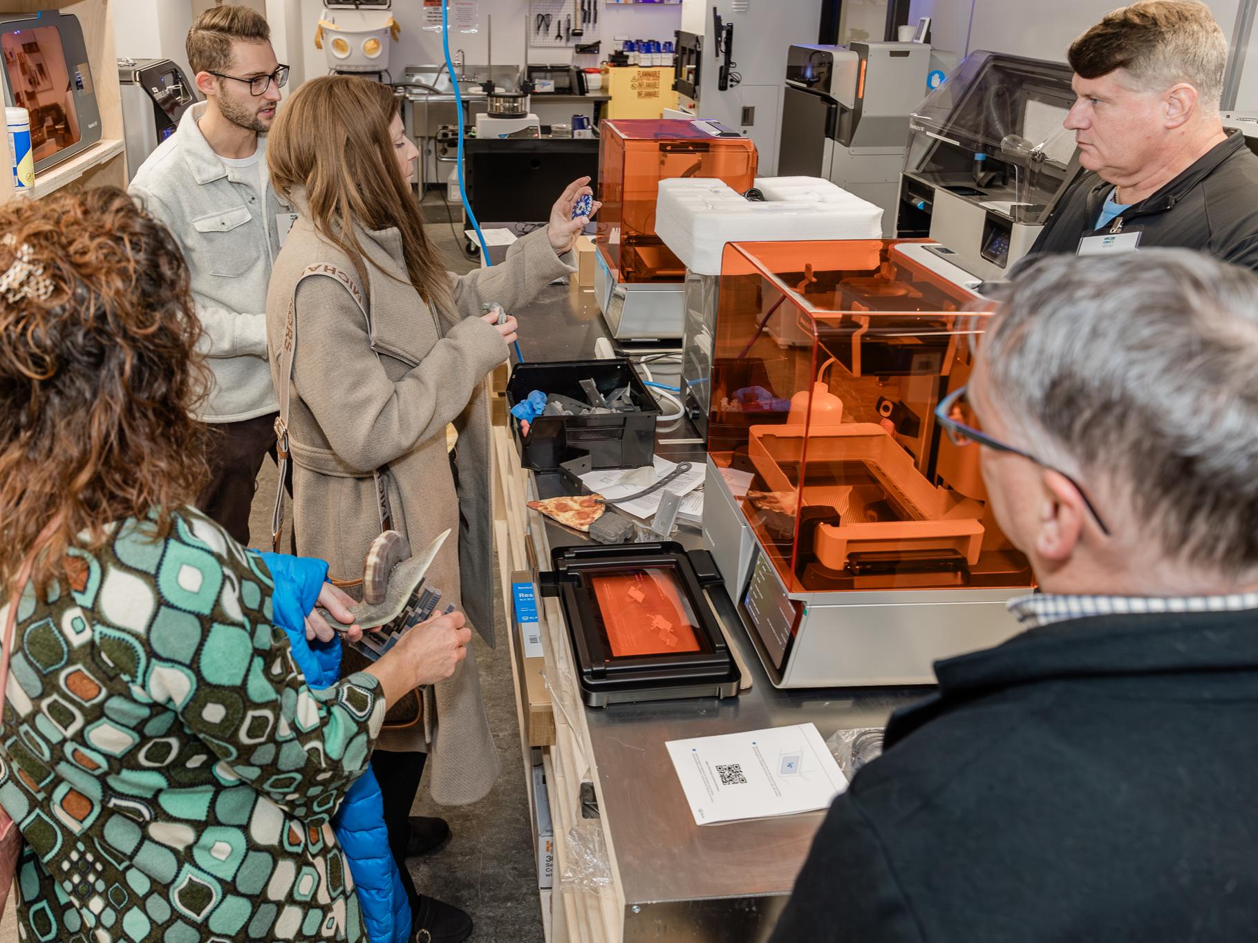 Four people on a tour guided by one individual of OriginLabs, looking at 3D printers and 3D-printed objects