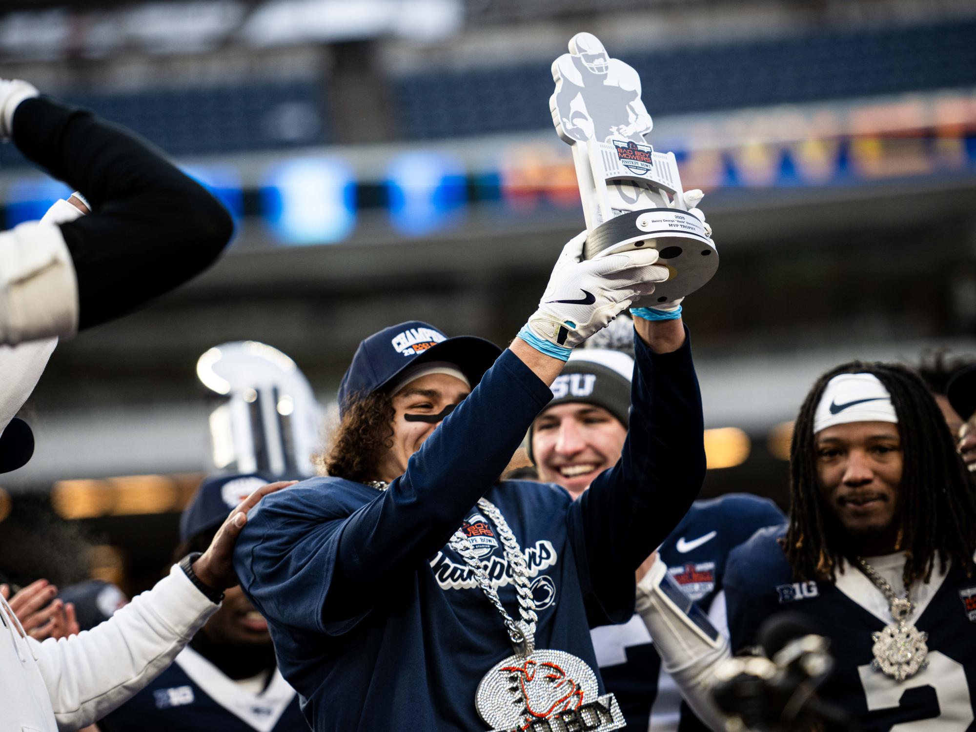 A football player holds up a MVP championship trophy in a large crowd.