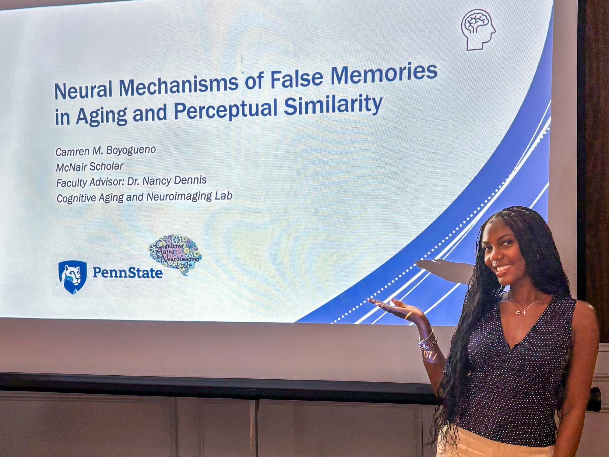 Camren Boyogueno stands in front of a large presentation screen giving a talk at Penn State. The slide behind her displays the Penn State mark and title of Camren’s talk.