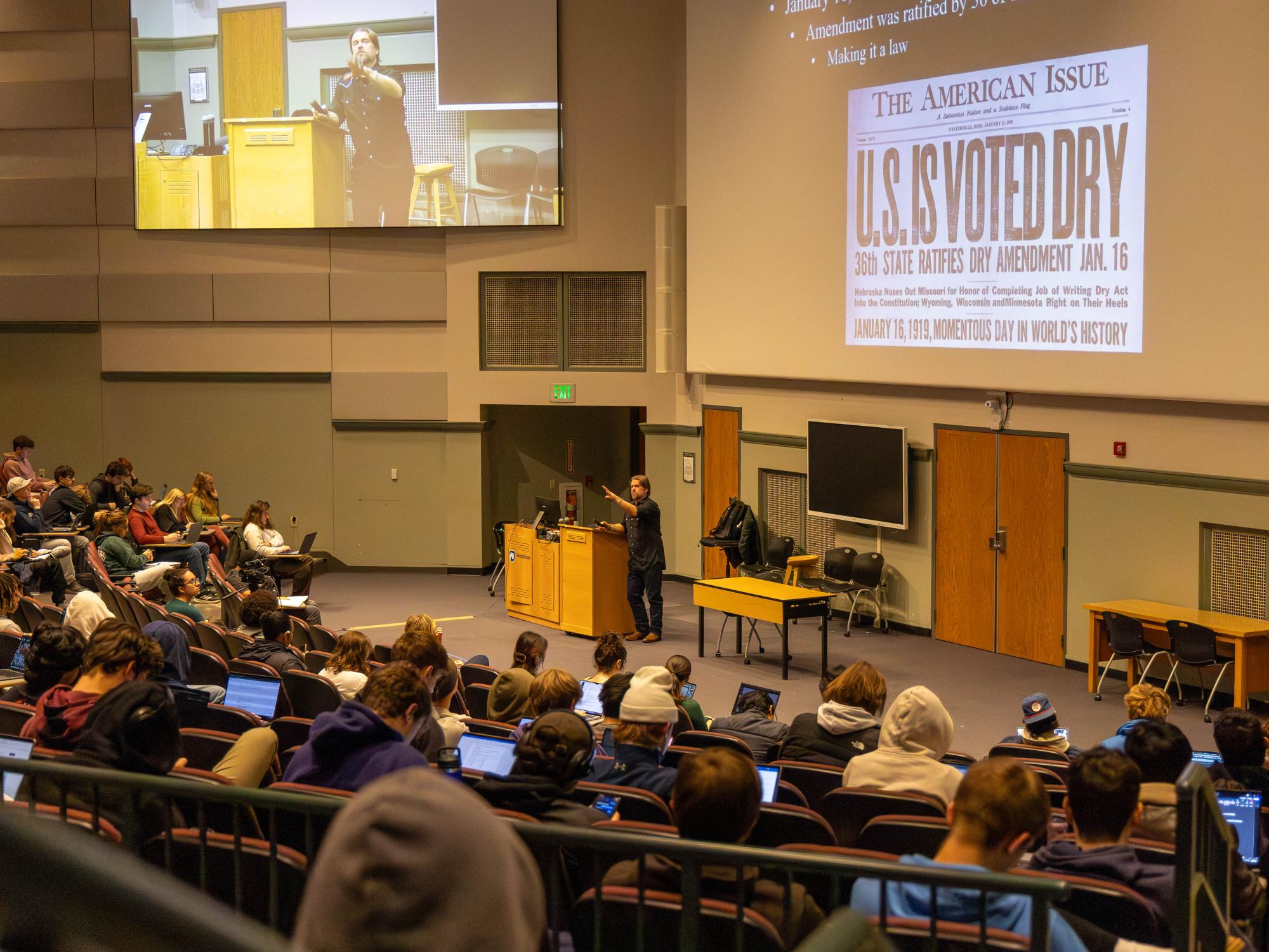 Kirk French lectures to his class with large projector screen in background 