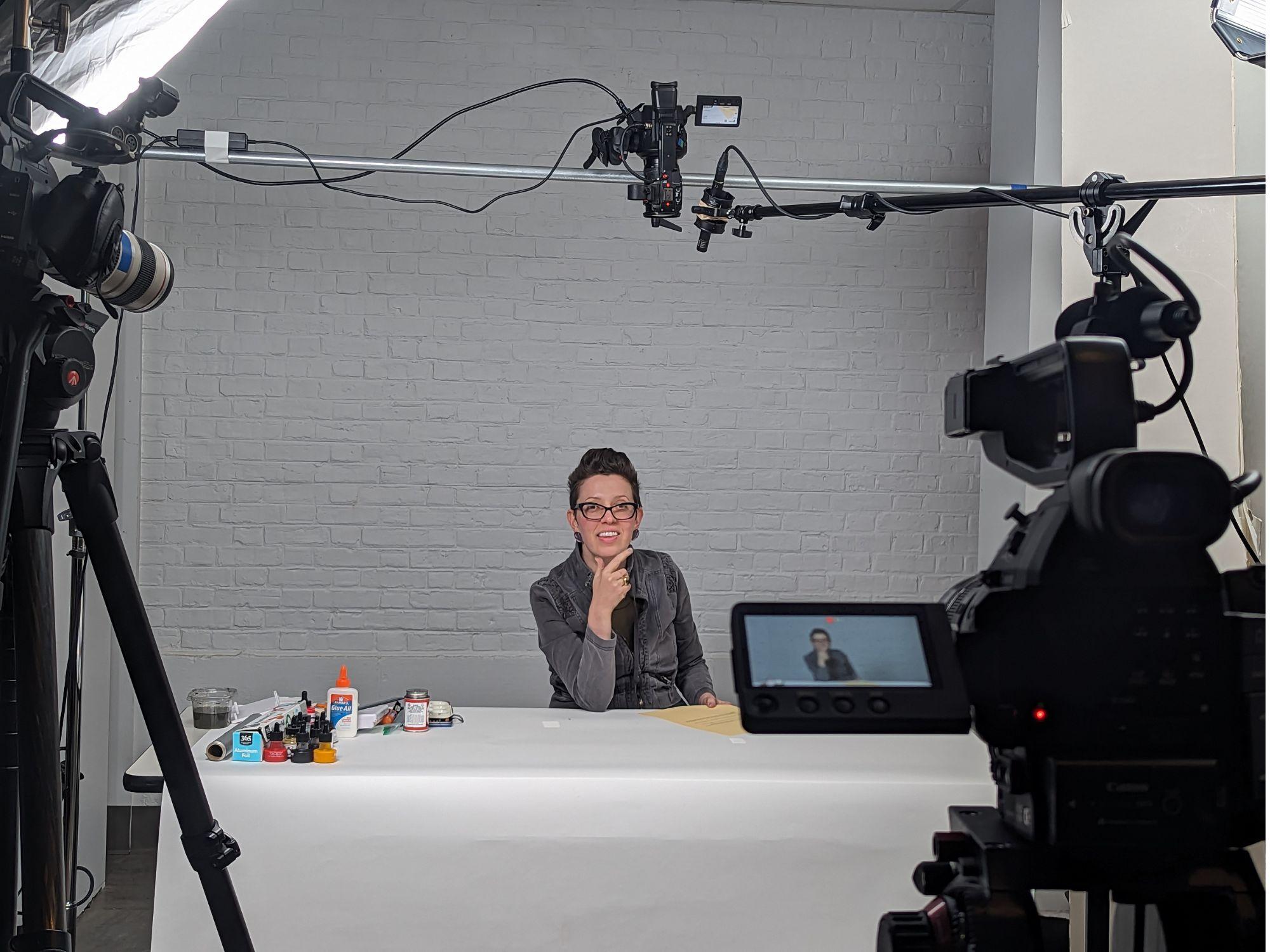 Anna Divinsky sits at a desk with a camera set up on her