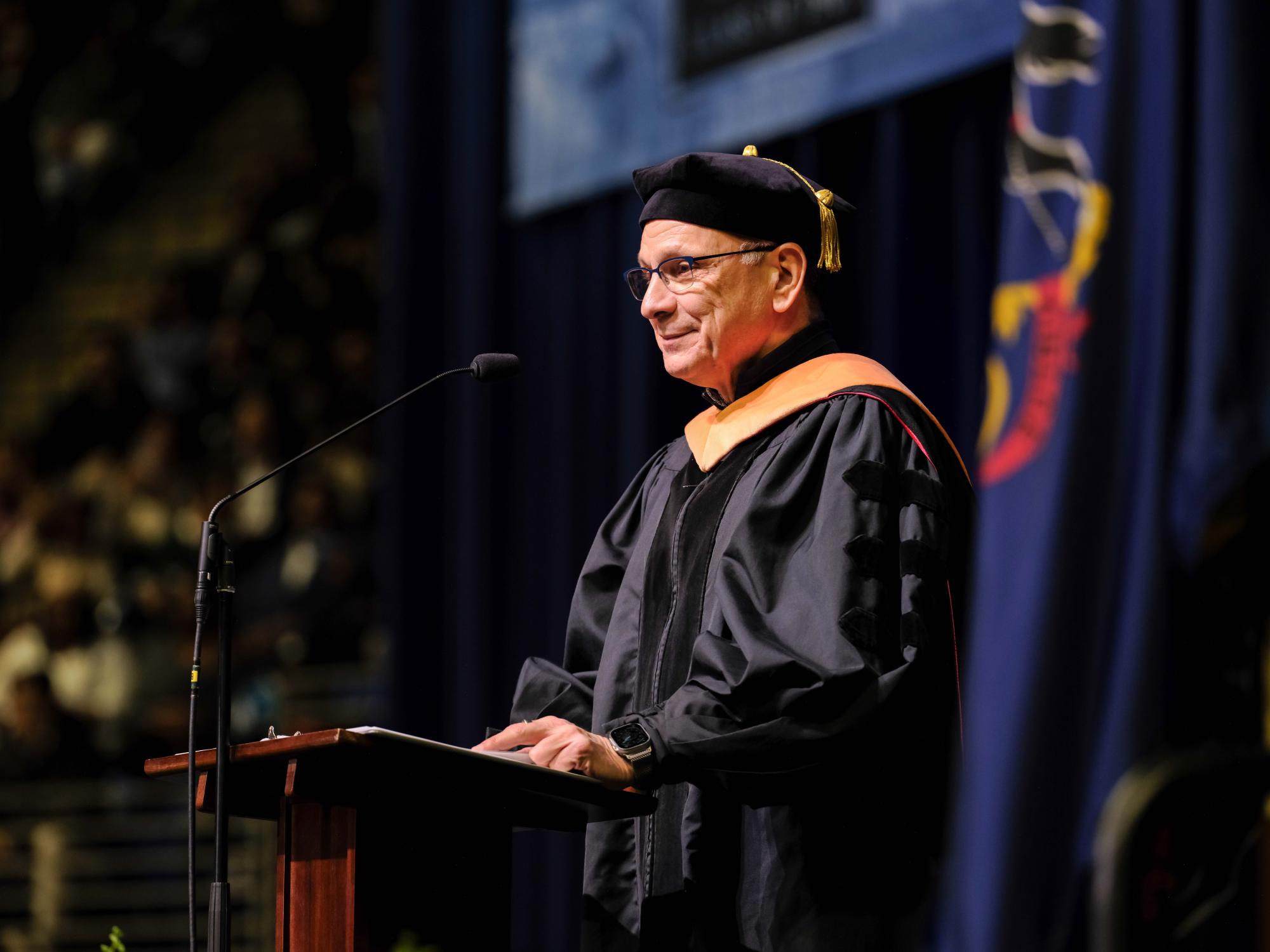 An university official speaks at by podium to a crowd 