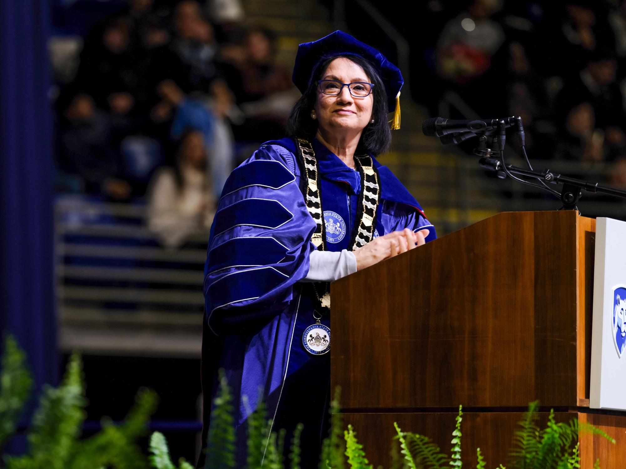 Penn State's President stands at a podium during a commencement ceremony, looking out toward the audience as she prepares to speak.