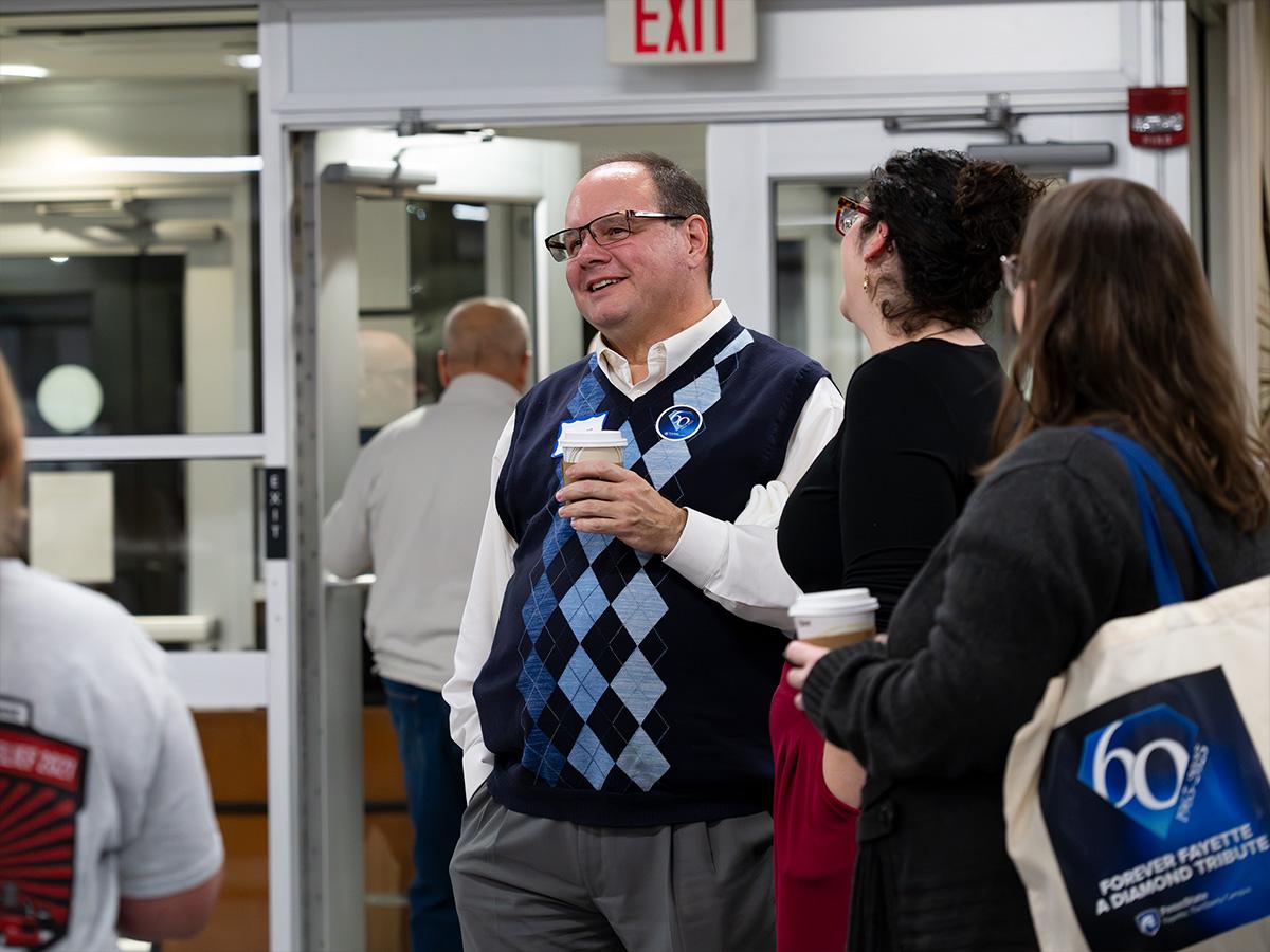A man holding a coffee cup speaks with guests near the entrance of the Williams Building during the celebration.