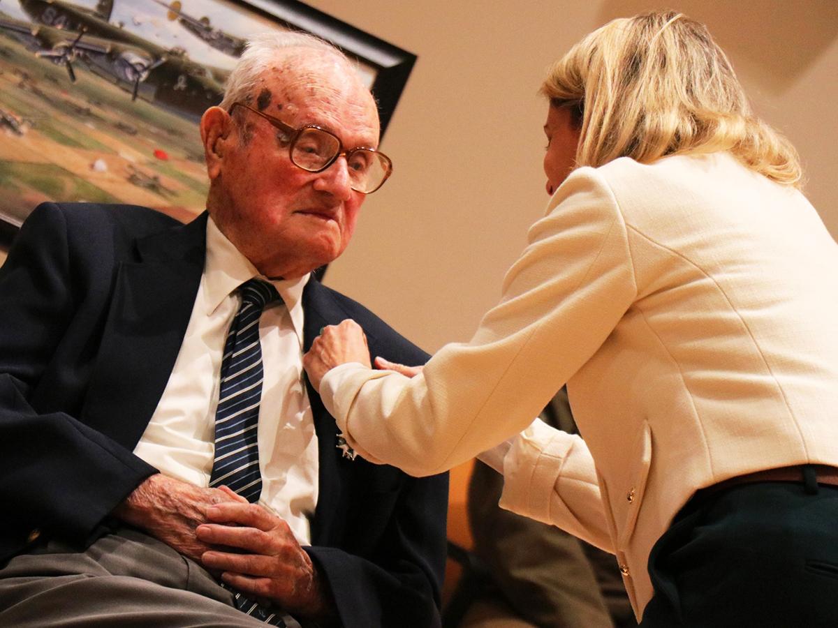 Caroline Monvoisin pins a medal onto John Homan's suit during a recognition ceremony.