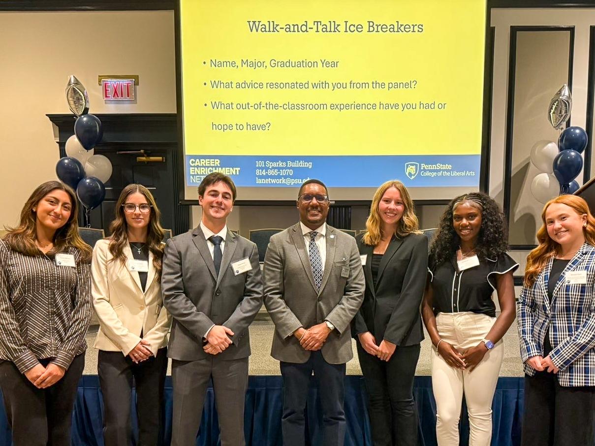 A group of students dressed in business attire posing together in front of a screen at a panel discussion.