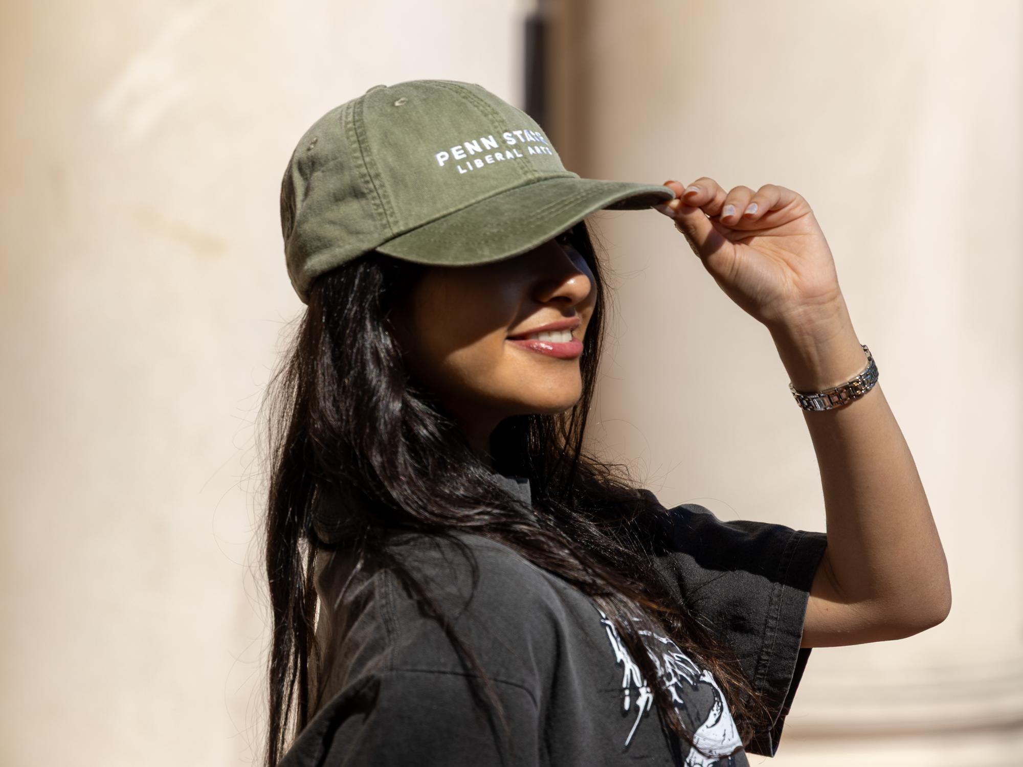 Maniar in front of Old Main pillars wearing a green Penn State College of the Liberal Arts baseball cap and black Old Coaly T-shirt.