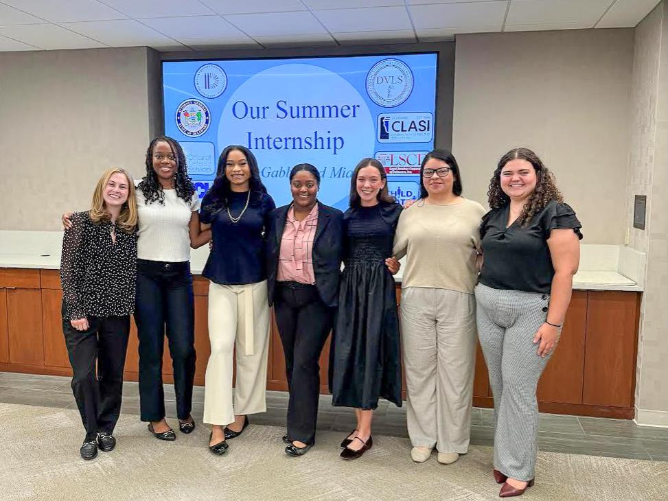 Gianna Martinelli (farthest to the left) with six others interns at Delaware Volunteer Legal Services in front of a projector screen that reads “Our Summer Internship.”