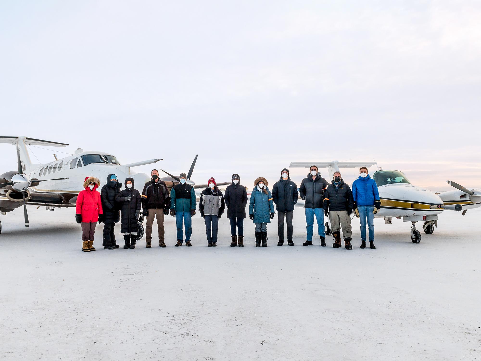 Researchers stand in the snow in front of two research aircraft