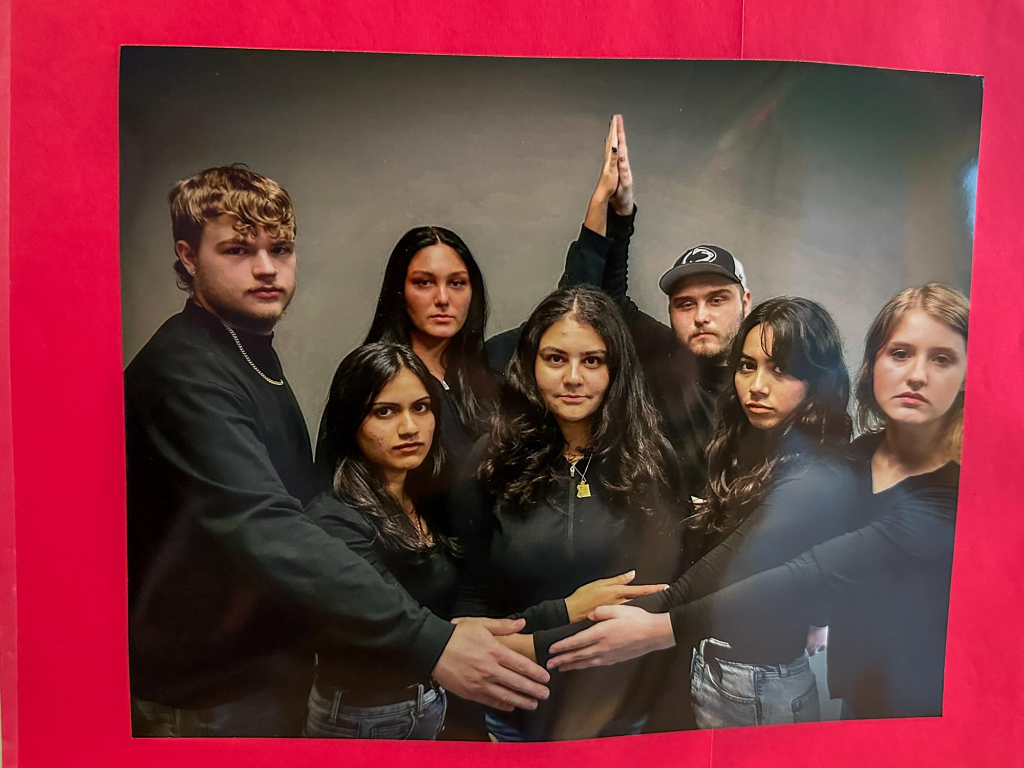 Seven students all wearing black shirts pose in an awkward photos with very serious expressions