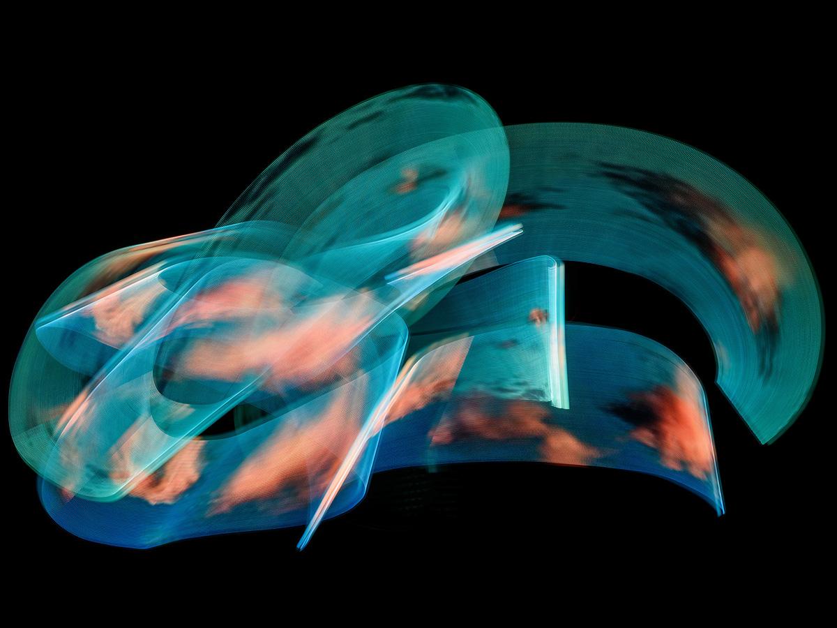 A long-exposure light drawing featuring broad teal arcs and soft orange cloudlike textures against a black background.