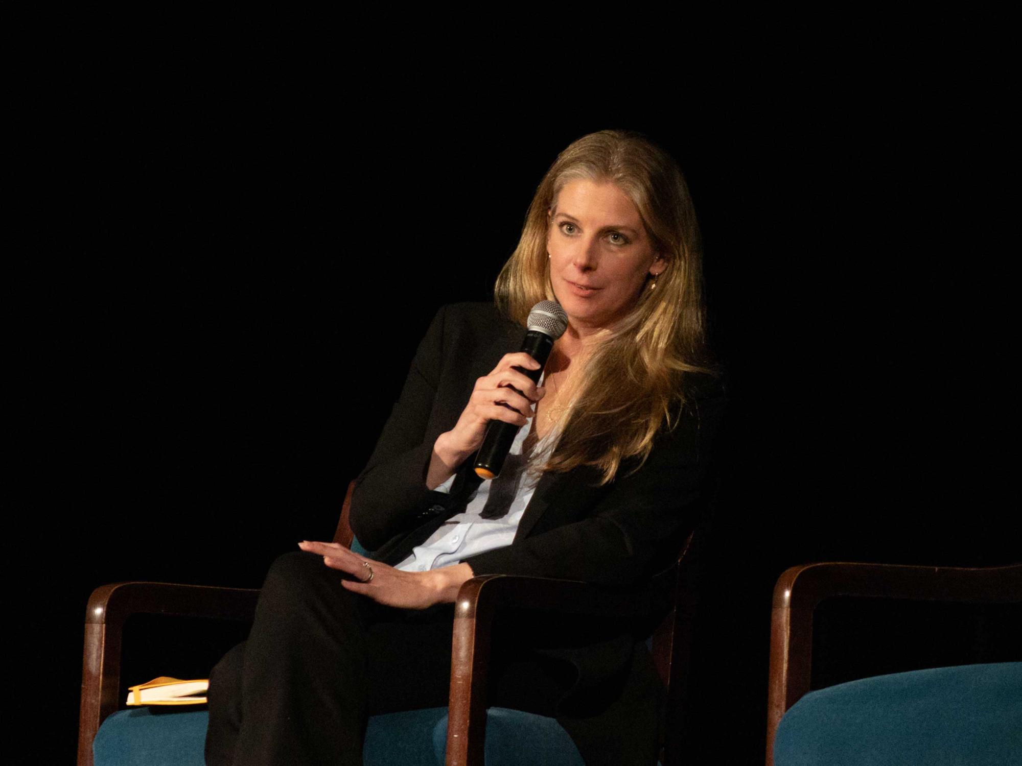 Nadia Drake sits in chair on stage and holds microphone