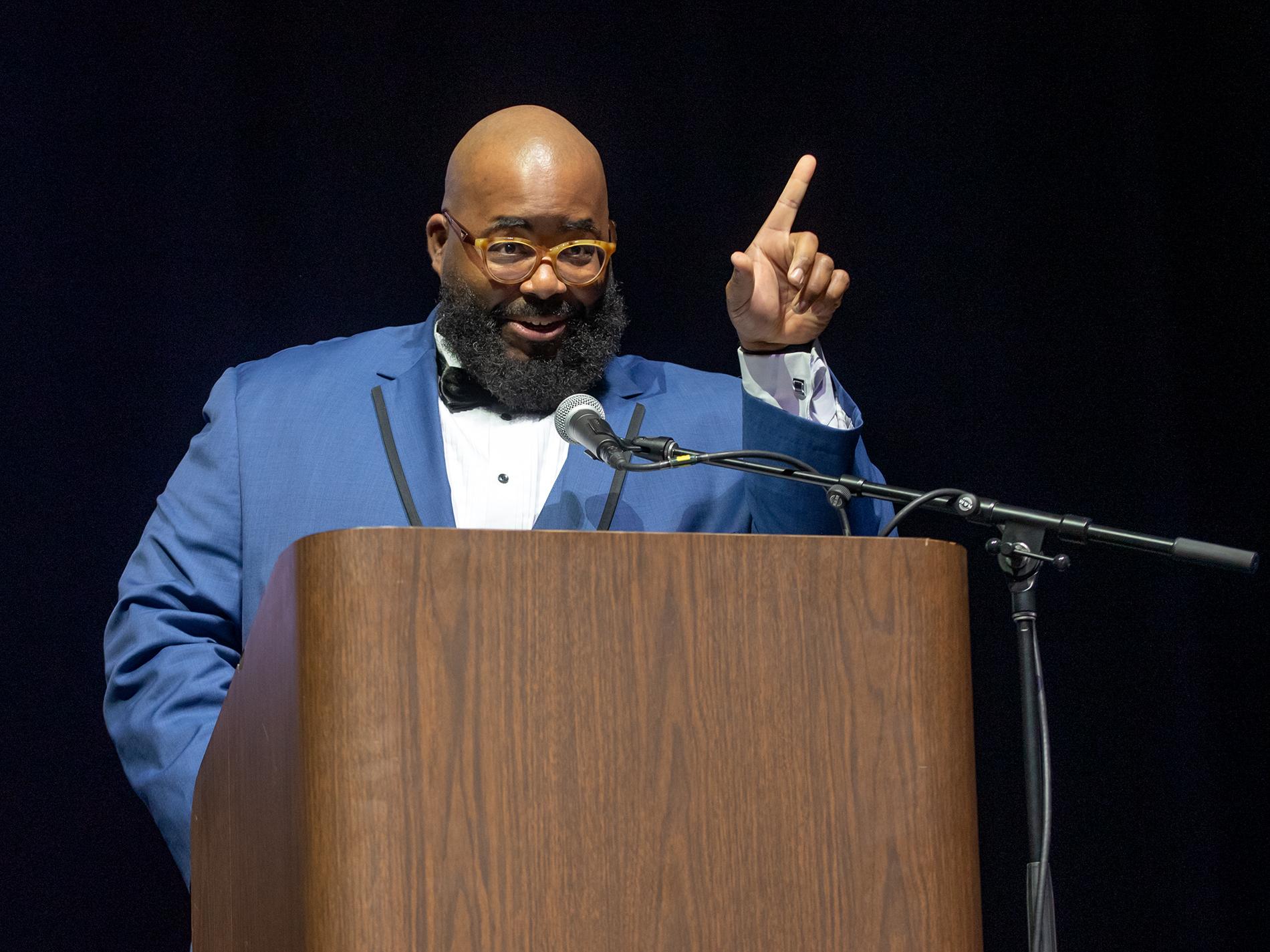 Evan Williams, in a blue suit, interacts with the audience as he speaks from a podium.