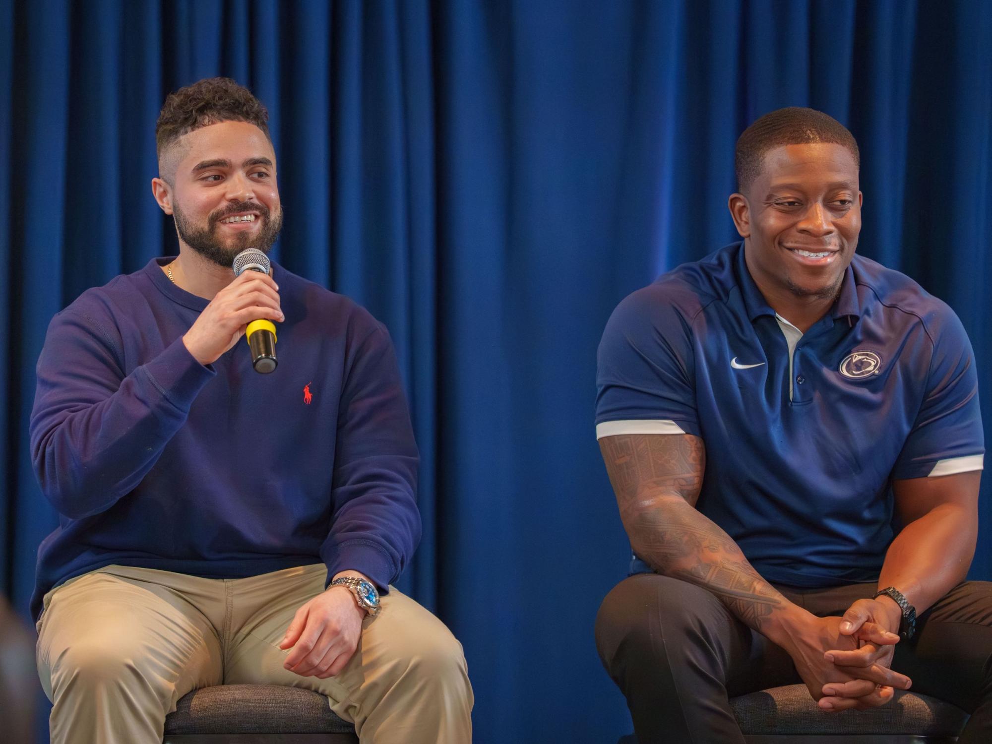 one smiling person holding microphone and seated next to another smiling person
