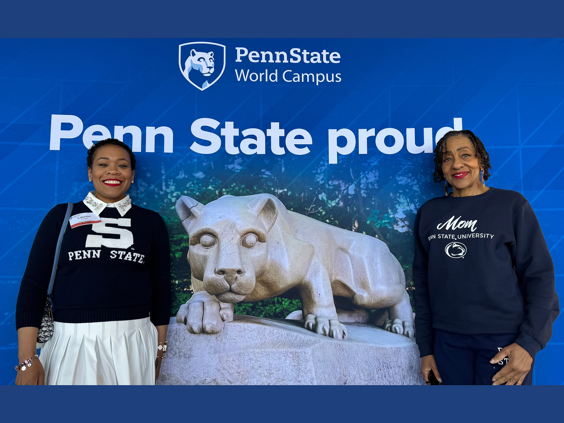 Two women pose in front of a Penn State photo background.
