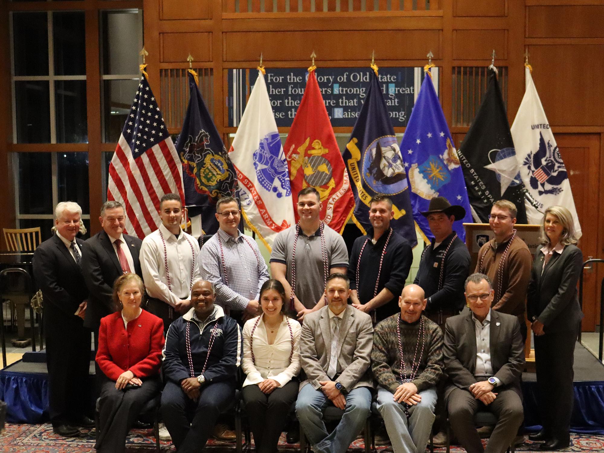 A group of people pose in front of the American flag and U.S. military flags.