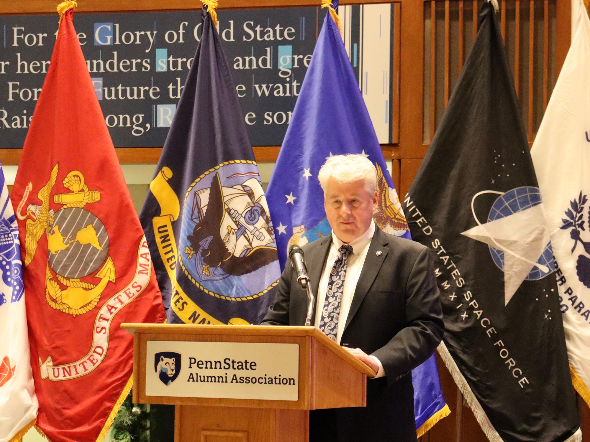 A man speaks at a podium in front of a group of flags.