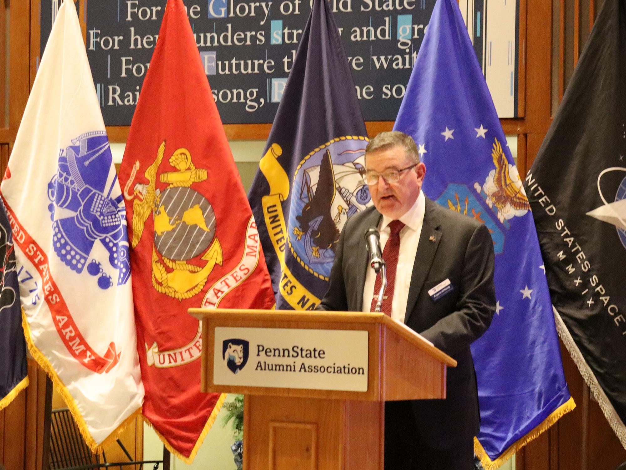 A man speaks at a podium in front of a group of flags.