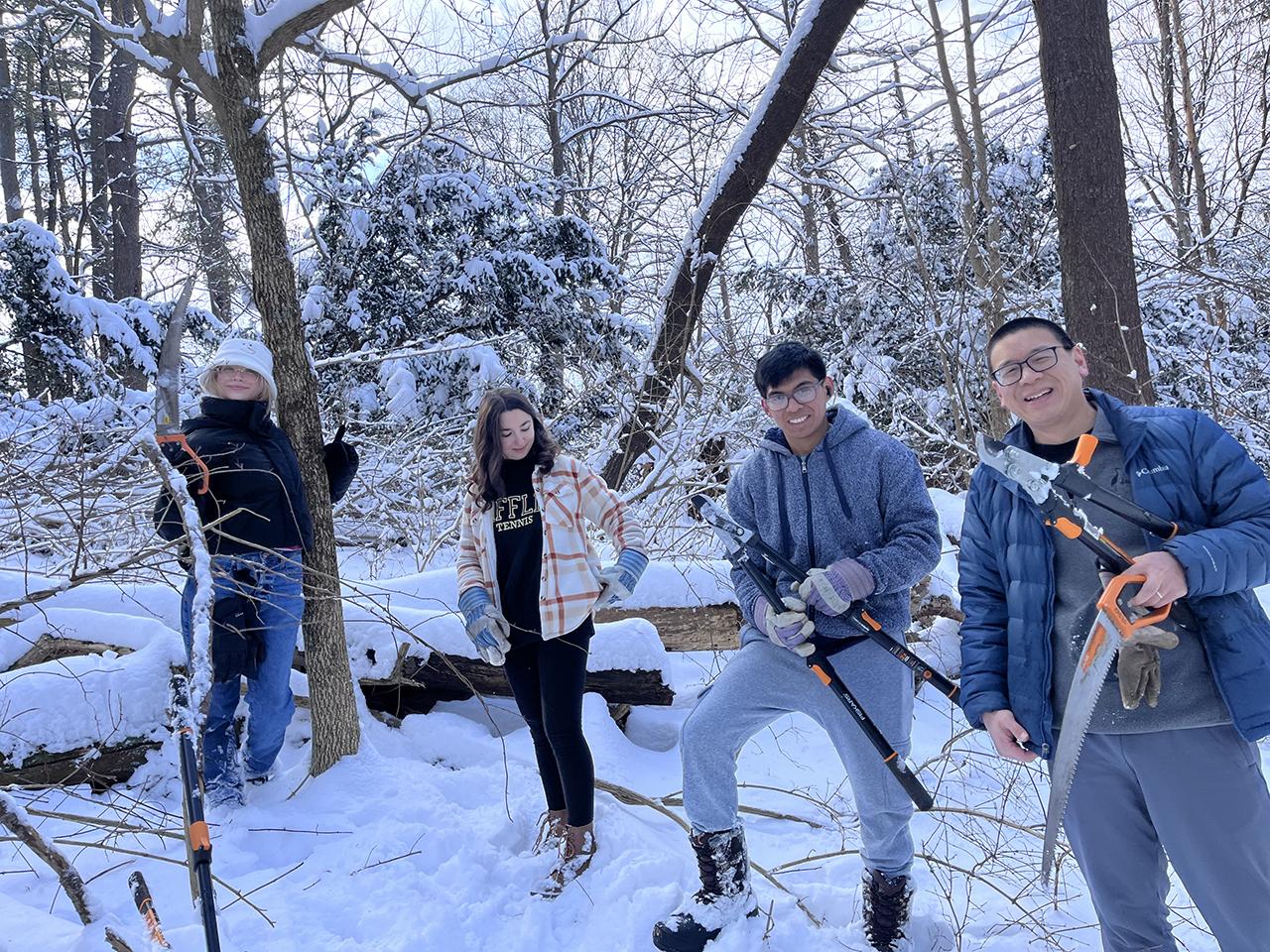 Three students and a faculty member stand in a snowy landscape holding gardening tools