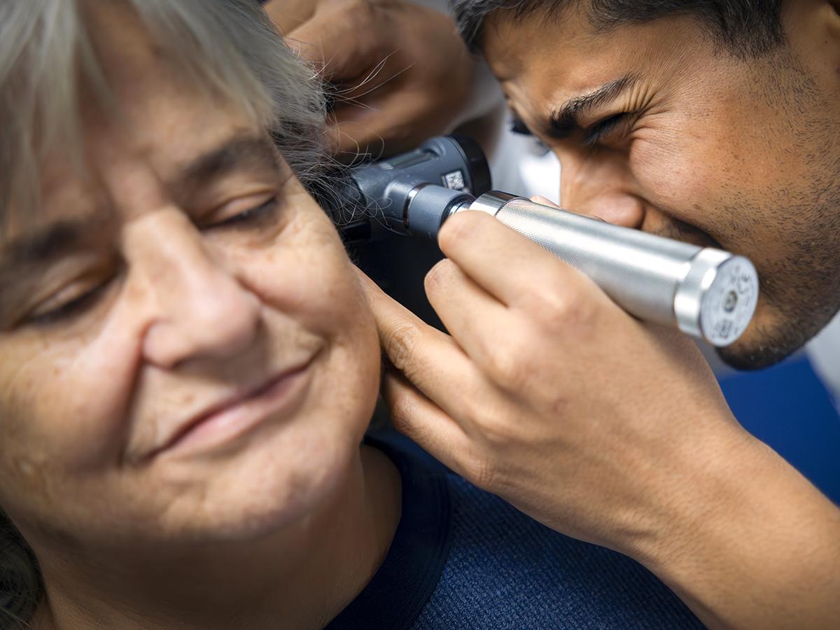 A doctor looks through an otoscope to examine a woman patient’s inner ear. 