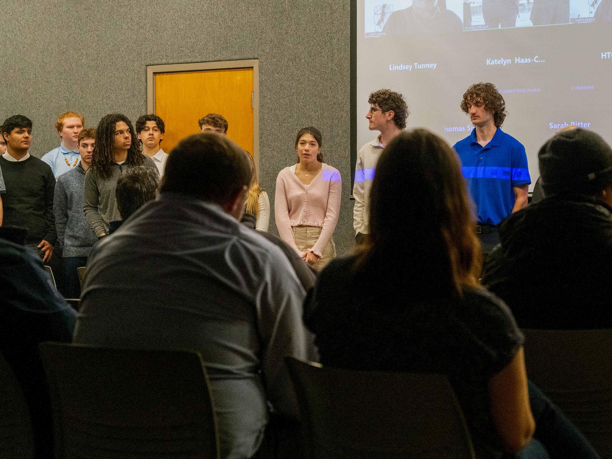 A young woman stands beside her fellow engineering students, fielding questions from audience members.