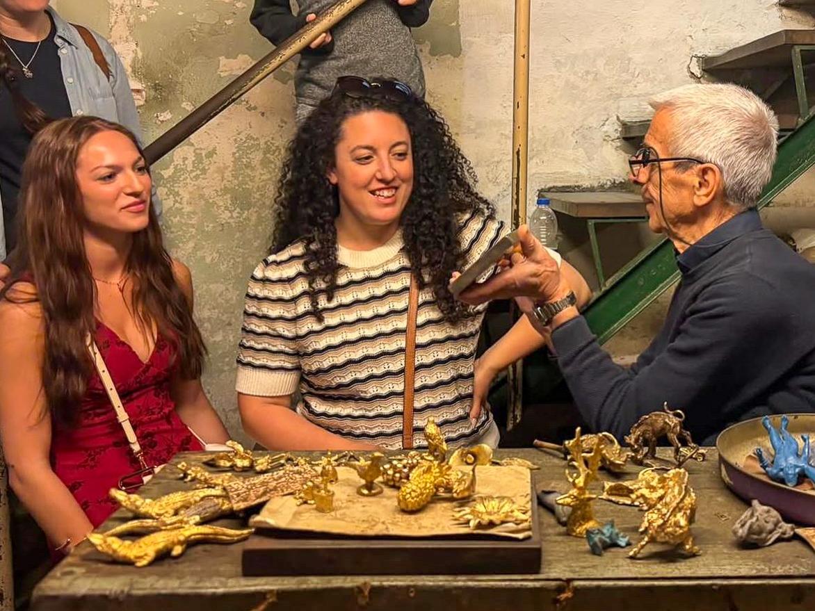 Alexis Wilson and Lauren Halberstadt speak to a man holding a cell phone, with figurines scattered on a table. 