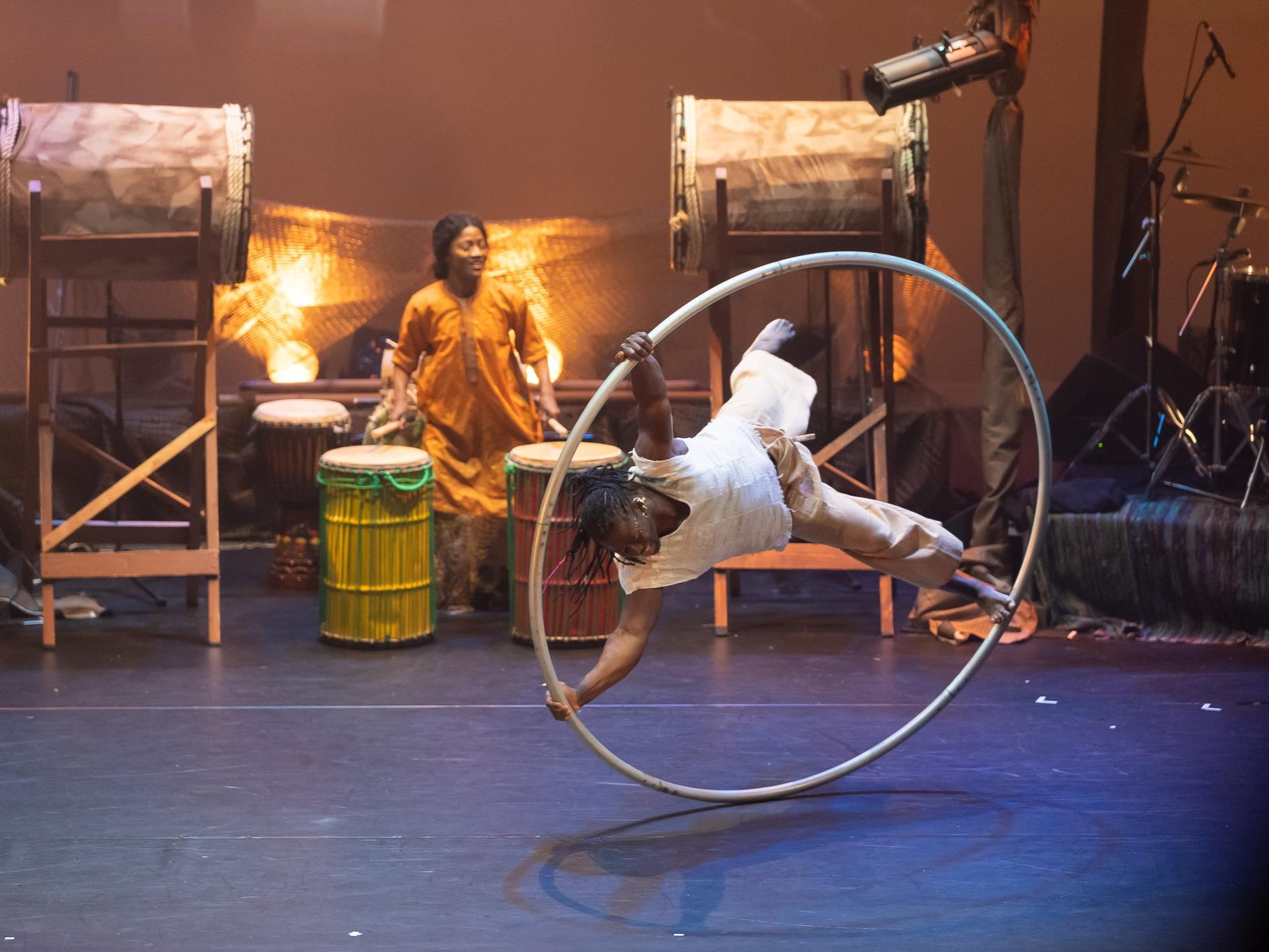 A Black man holds on to a large hoop as he rolls on a stage.