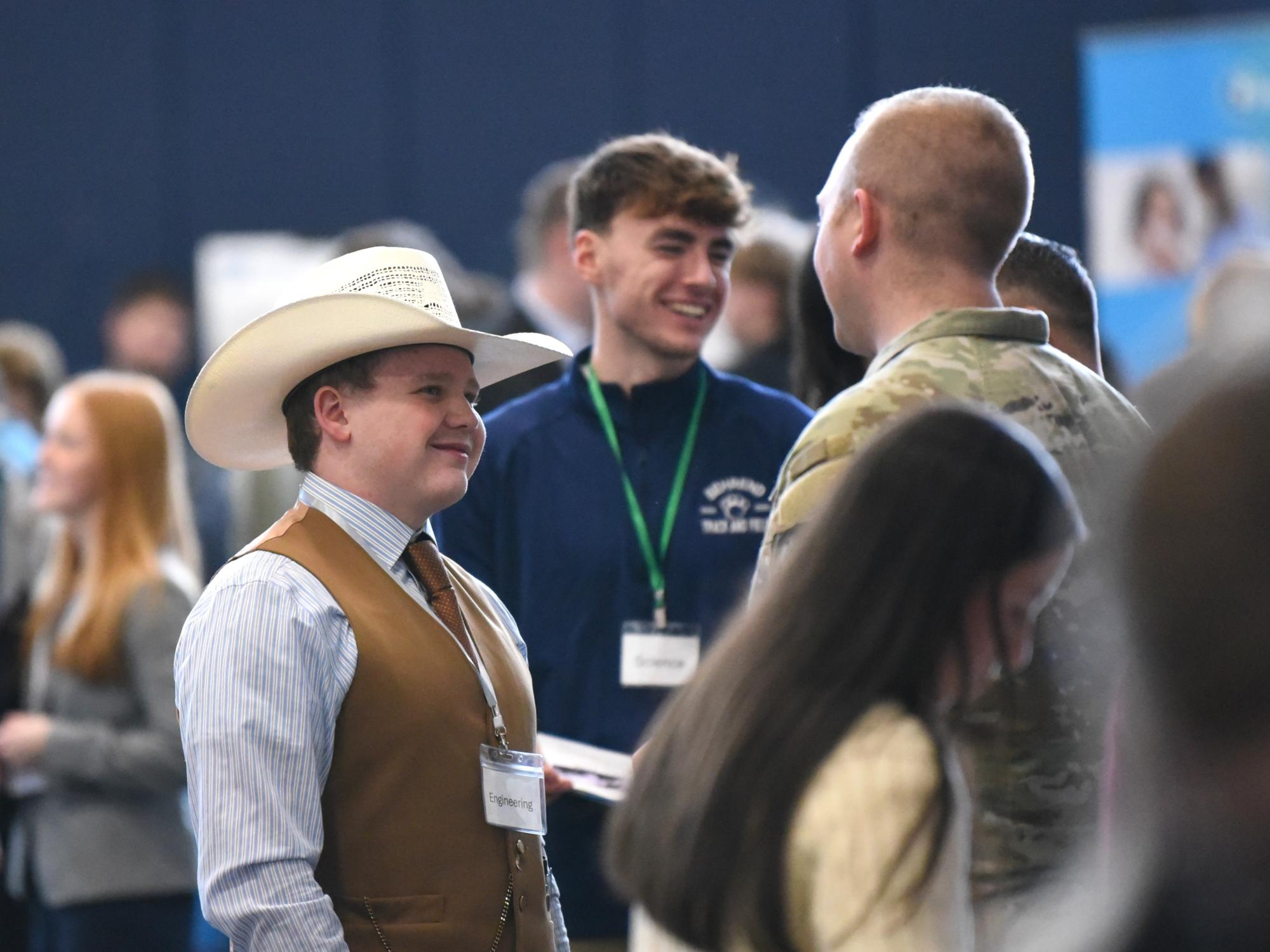 A student in a cowboy hat talks to a military recruiter at Penn State Behrend's career fair.
