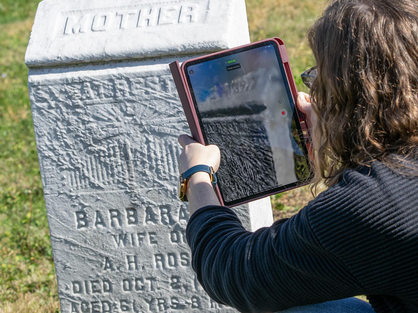 Mariah Kupfner uses a tablet to 3D scan a headstone in a cemetery 