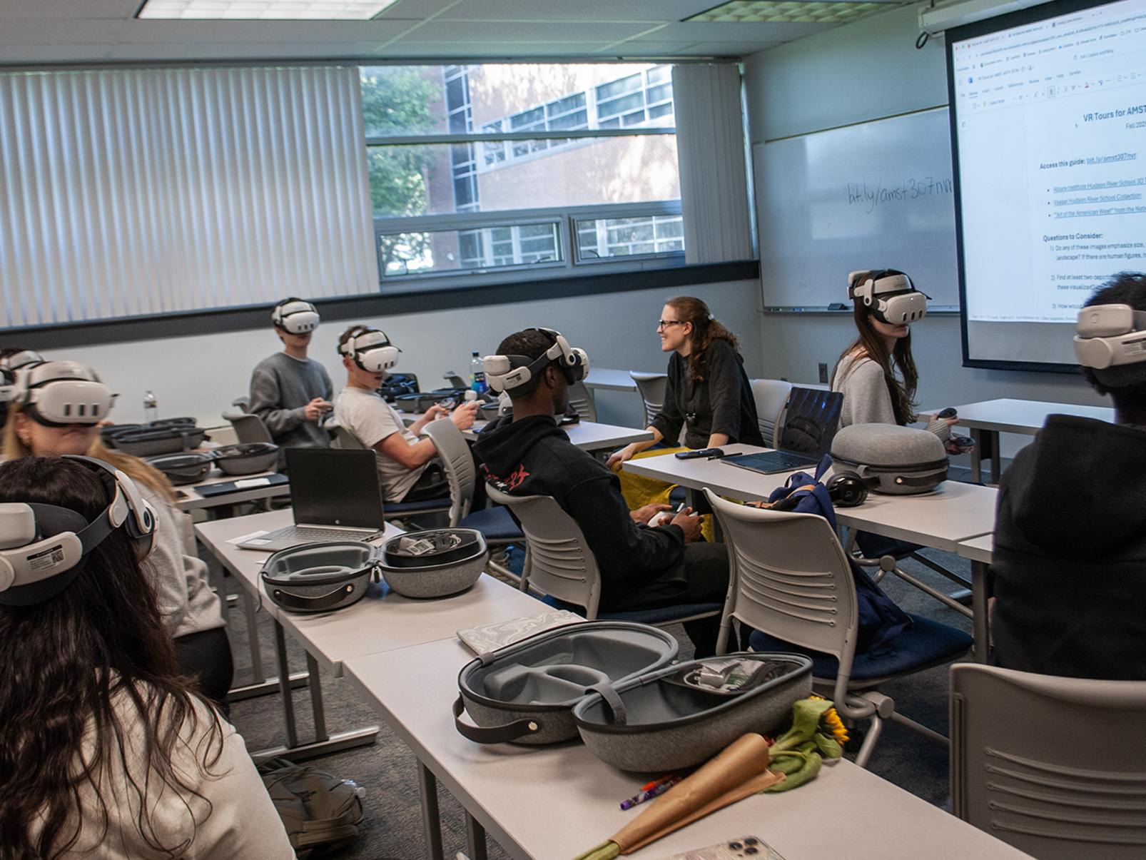 Students sit at long tables in a classroom wearing virtual reality headsets