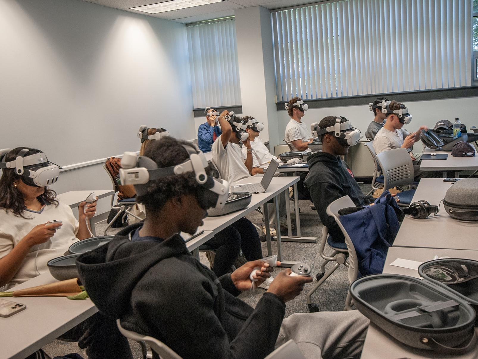Students in a classroom wear virtual reality headsets and hold remote controls