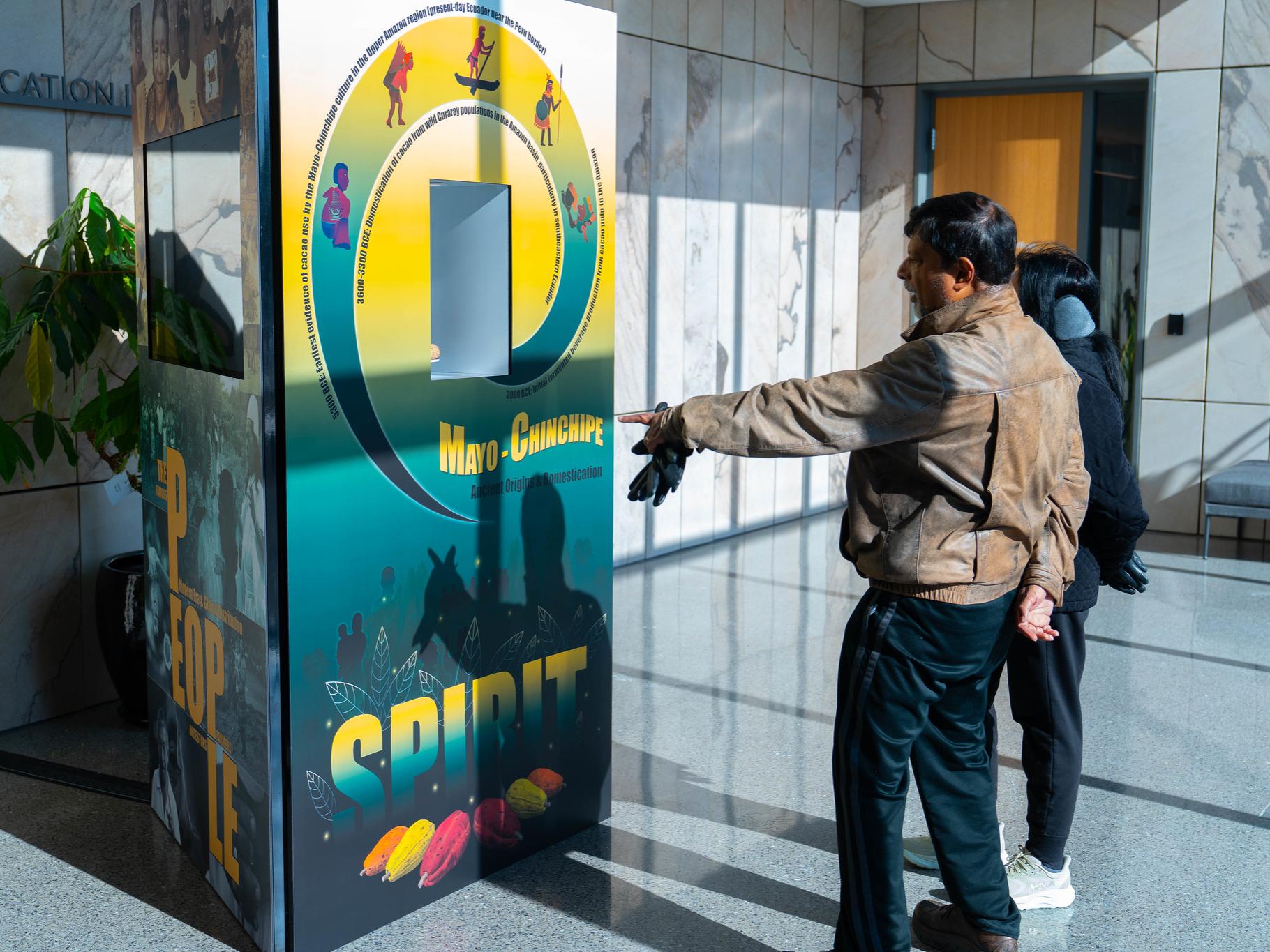 Two people looking at an exhibit about chocolate; one of them points at the exhibit