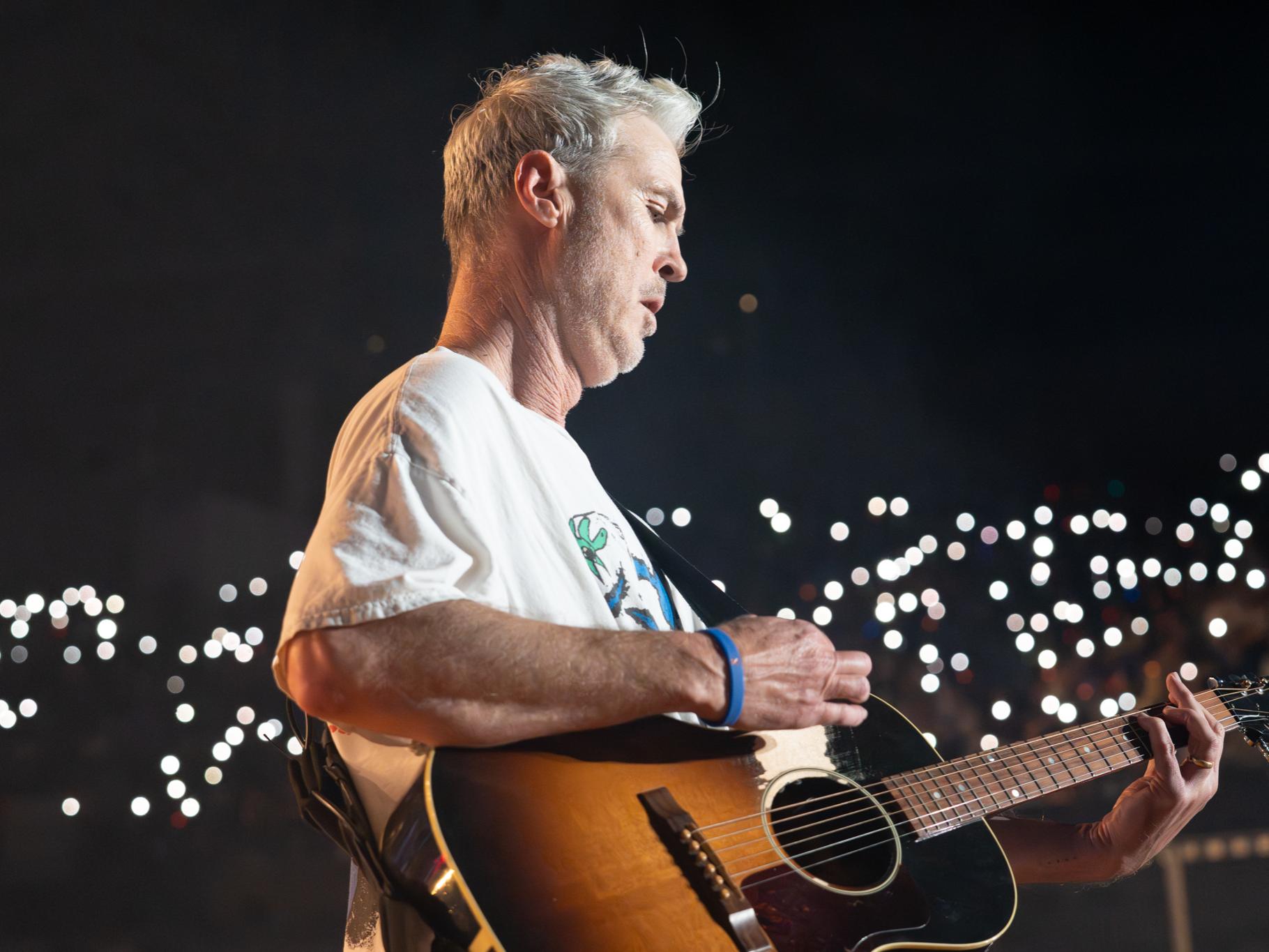 A person playing the guitar with phone flashlights shining in the back