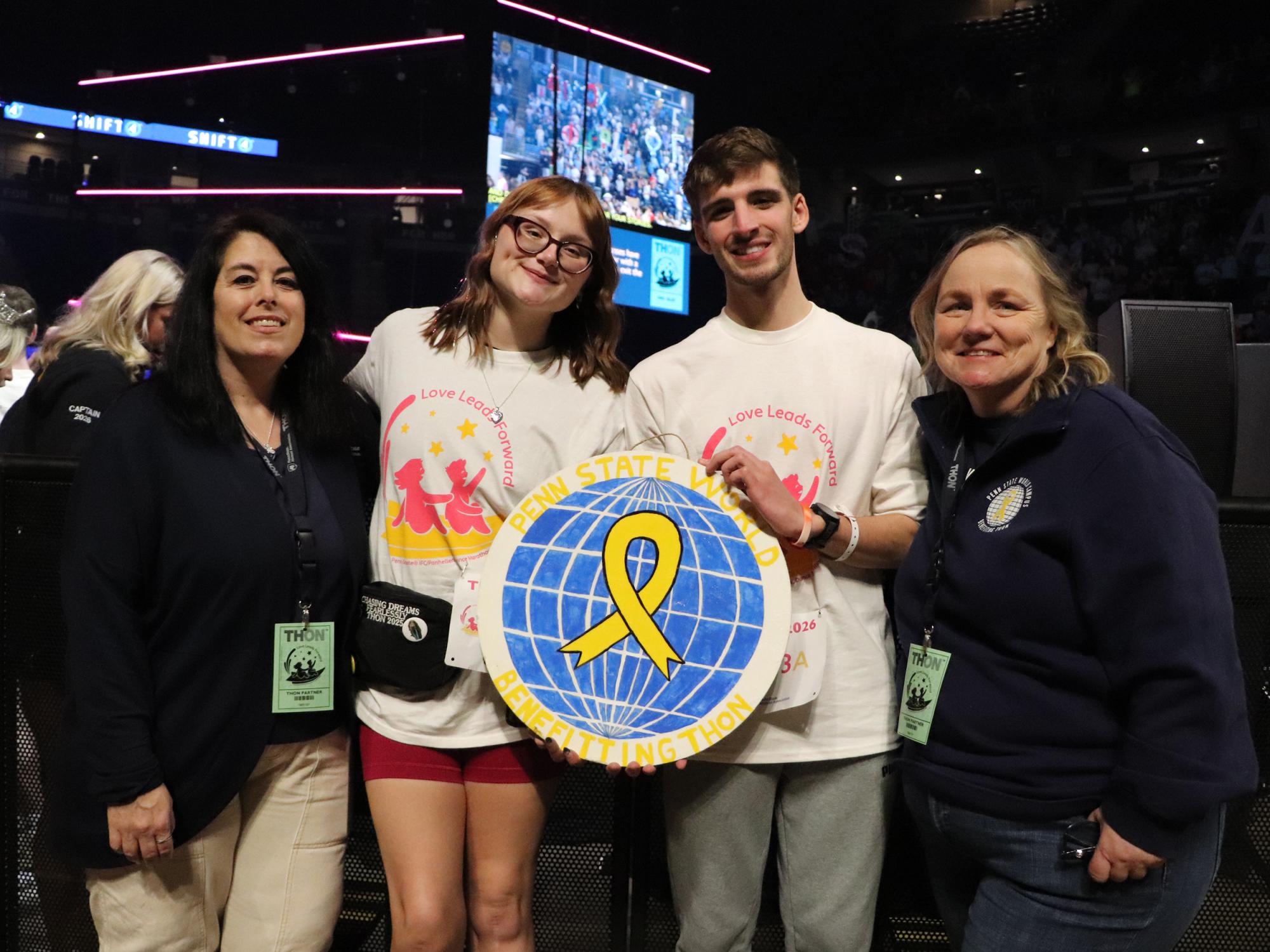 Four people pose with logo in an arena.
